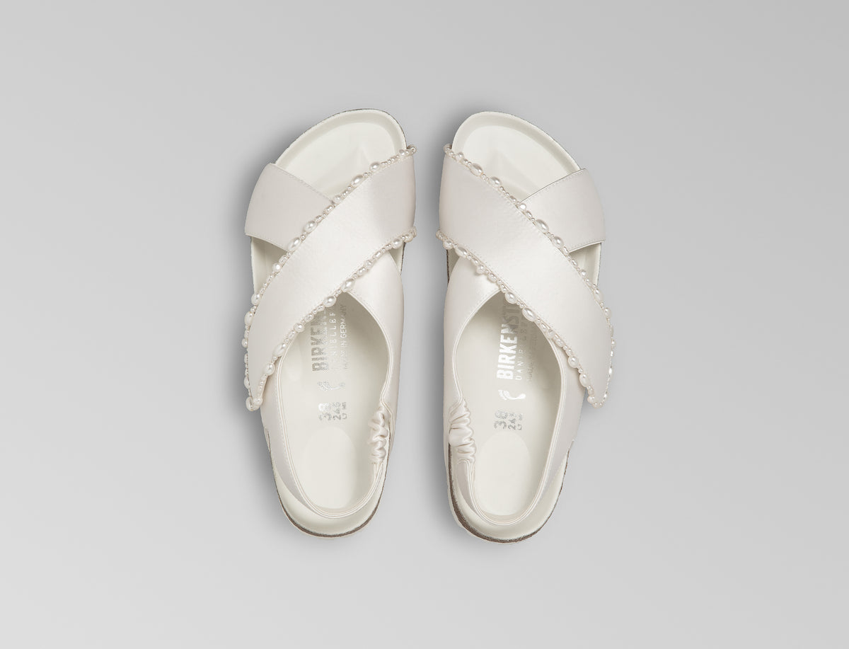 The Tulum is reimagined in a luminous ivory satin, featuring a graceful crossover profile and a slim ankle strap adorned with delicate pearls. The design also introduces an innovative adjustable hidden buckle closure. Handcrafted in Germany, the shoe merges BIRKENSTOCK’s legendary comfort with Danielle Frankel’s signature touch of refined elegance.- Upper: Delicate satin upper, naturally shaped pearls handstitched on trim- Footbed: Anatomical shaped BIRKENSTOCK cork latex Footbed lined with premium Nappa Leather- Sole: EVA die cut outsole with a custom design, blending classic BIRKENSTOCK bone pattern with delicate leaf inspired detailing