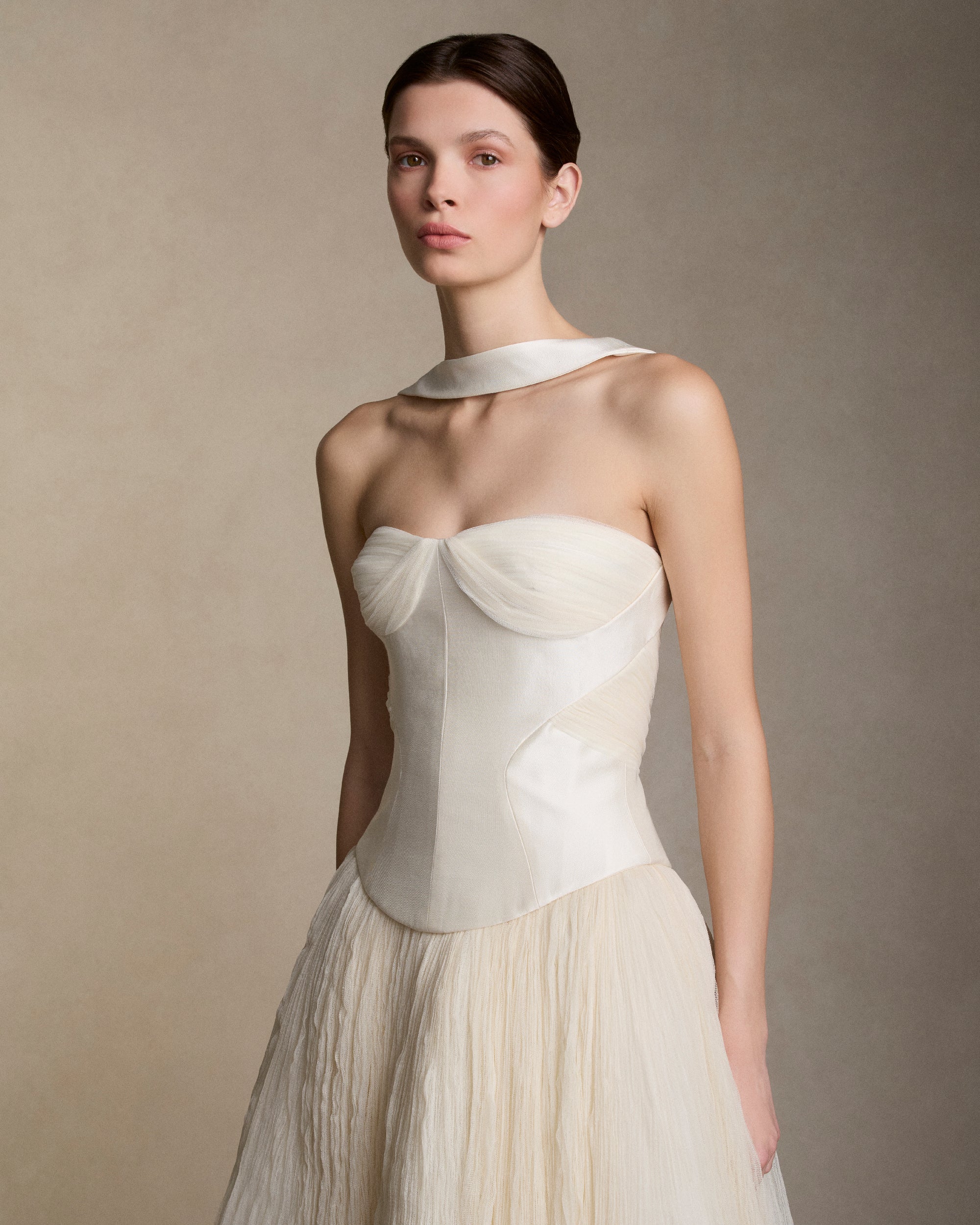 Silk wool twill bustier with curved shaped seams and attached neck wrap detail. Gathered and draped soft tulle frames the bust wrapping the body descending into tulle streamers at center back. Boned internal bustier, internal grosgrain belt and invisible zip closure at center back.Styled with Georgia Skirt