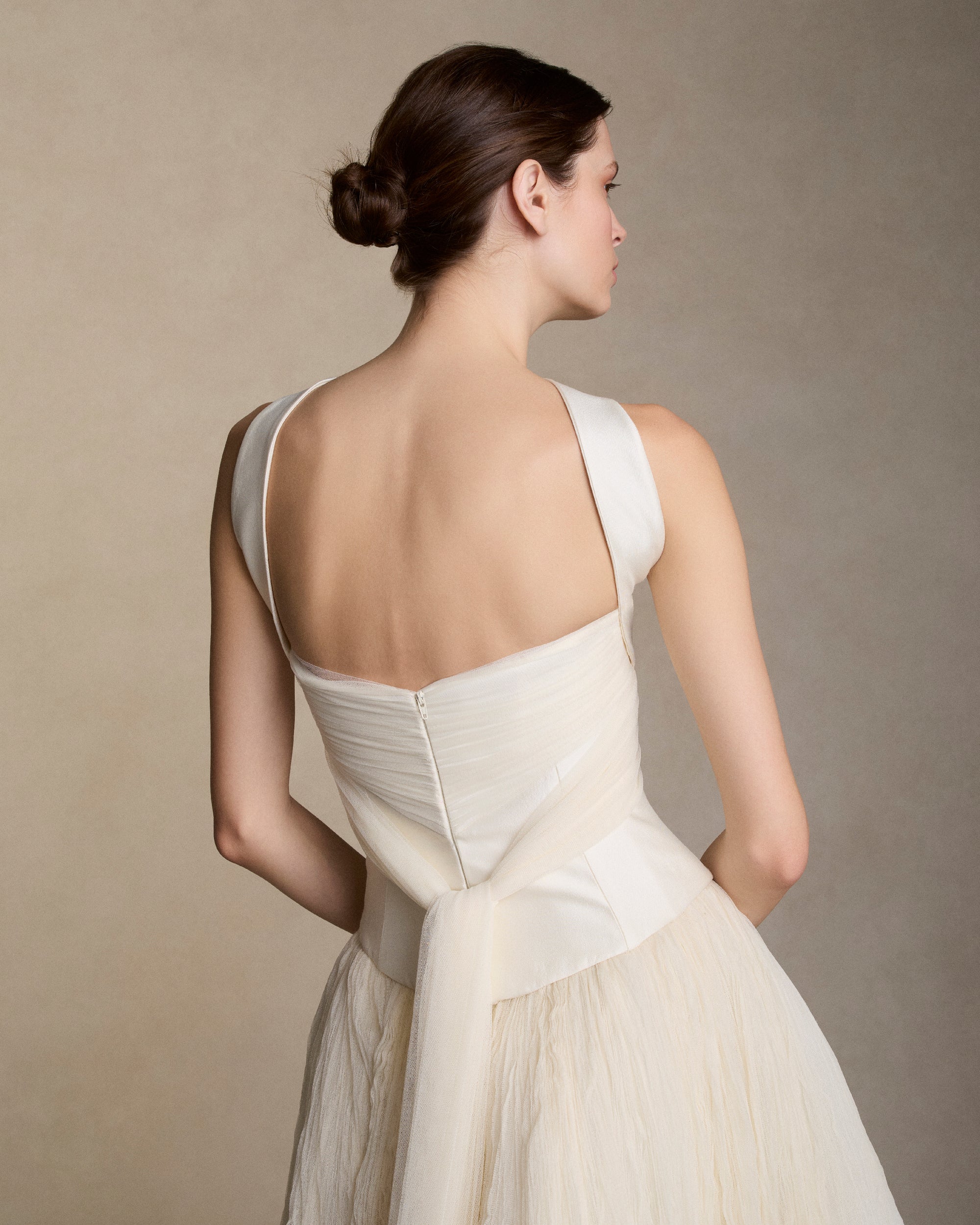 Silk wool twill bustier with curved shaped seams and attached neck wrap detail. Gathered and draped soft tulle frames the bust wrapping the body descending into tulle streamers at center back. Boned internal bustier, internal grosgrain belt and invisible zip closure at center back.Styled with Georgia Skirt
