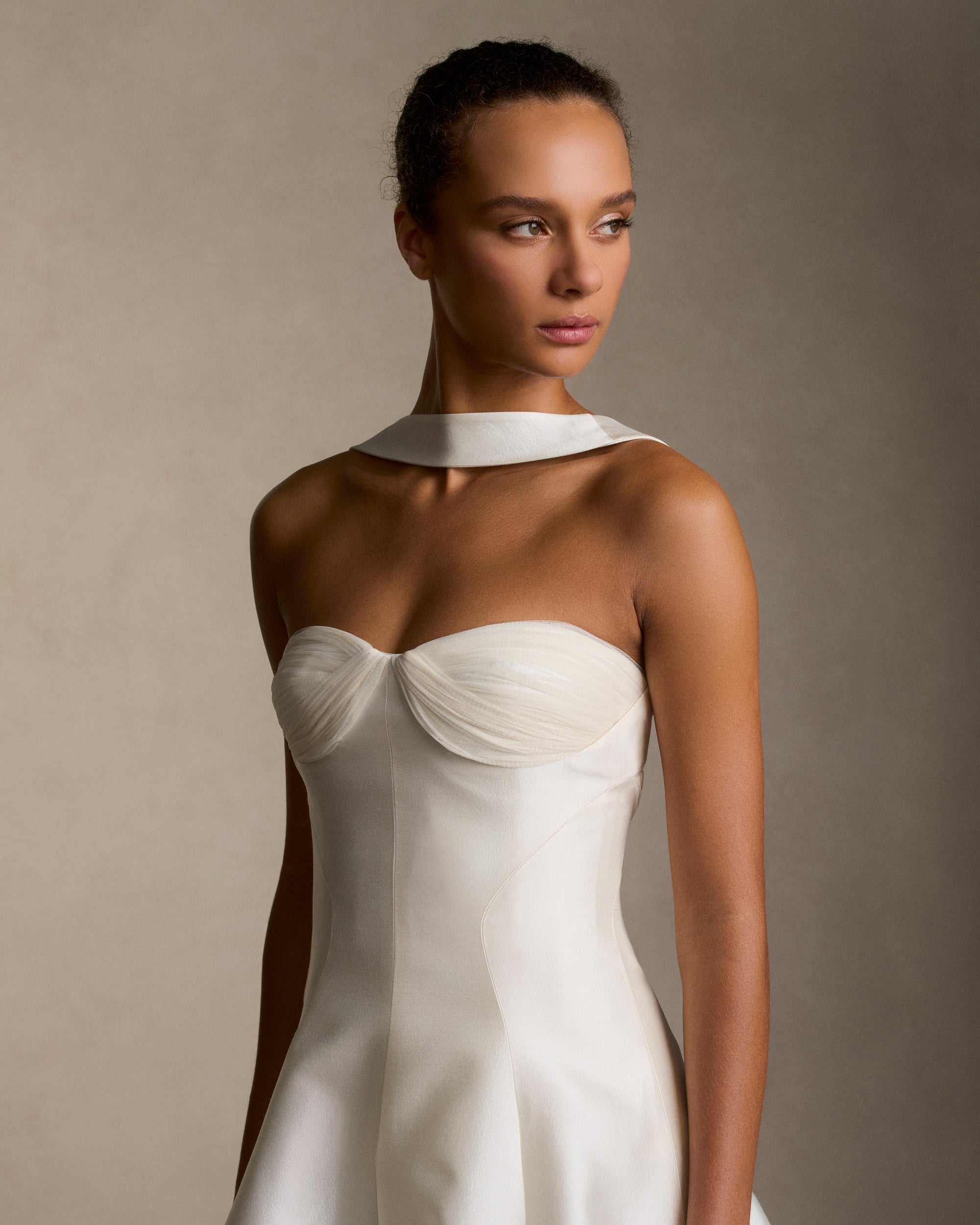 Silk wool twill ballgown with curved shaped seams and attached neck wrap detail. Gathered and draped tulle frames the bust wrapping towards the center back. Boned internal bustier, internal grosgrain belt and invisible zip closure at center back.