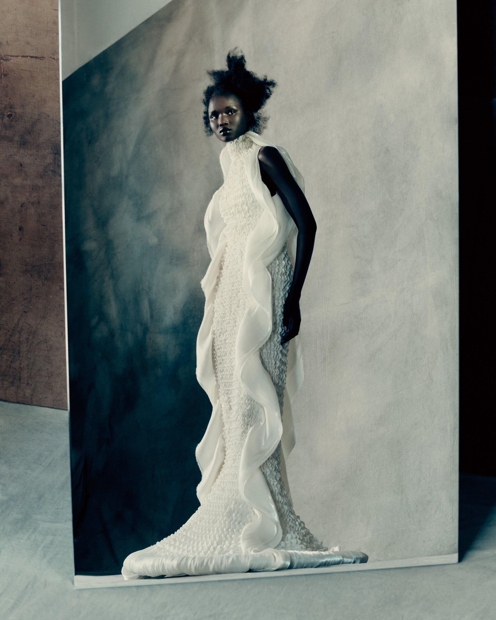 Smocked high-neck gown cut in luminous techno charmeuse. Engineered to shape the body, the smocking is finished with a cascading ribbon detail that frames the open back and traces the silhouette. Self fabric covered button closure at back neck and invisible zip at waist.