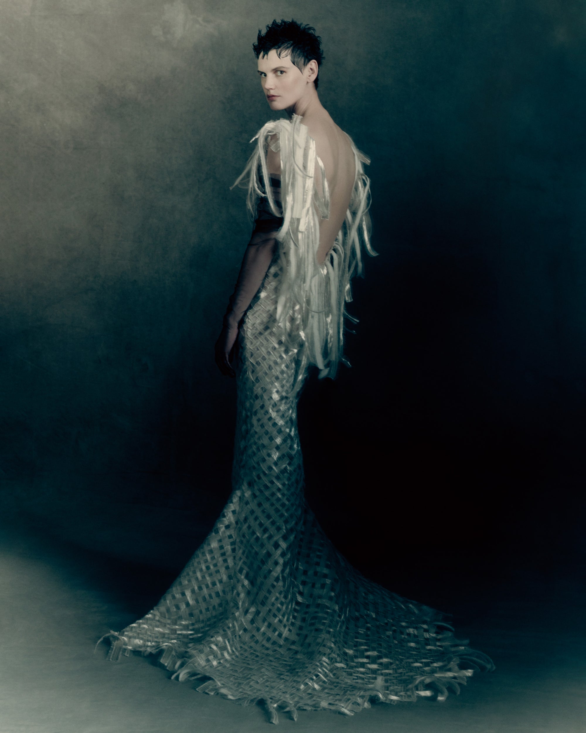 High-neck, V-back gown cut from pewter-toned woven silk and metal embroidery. Bias-cut ribbons are layered with hand-frayed organza, releasing into looped fringe at the neckline that falls down the center back. Invisible zip closure at center back. 