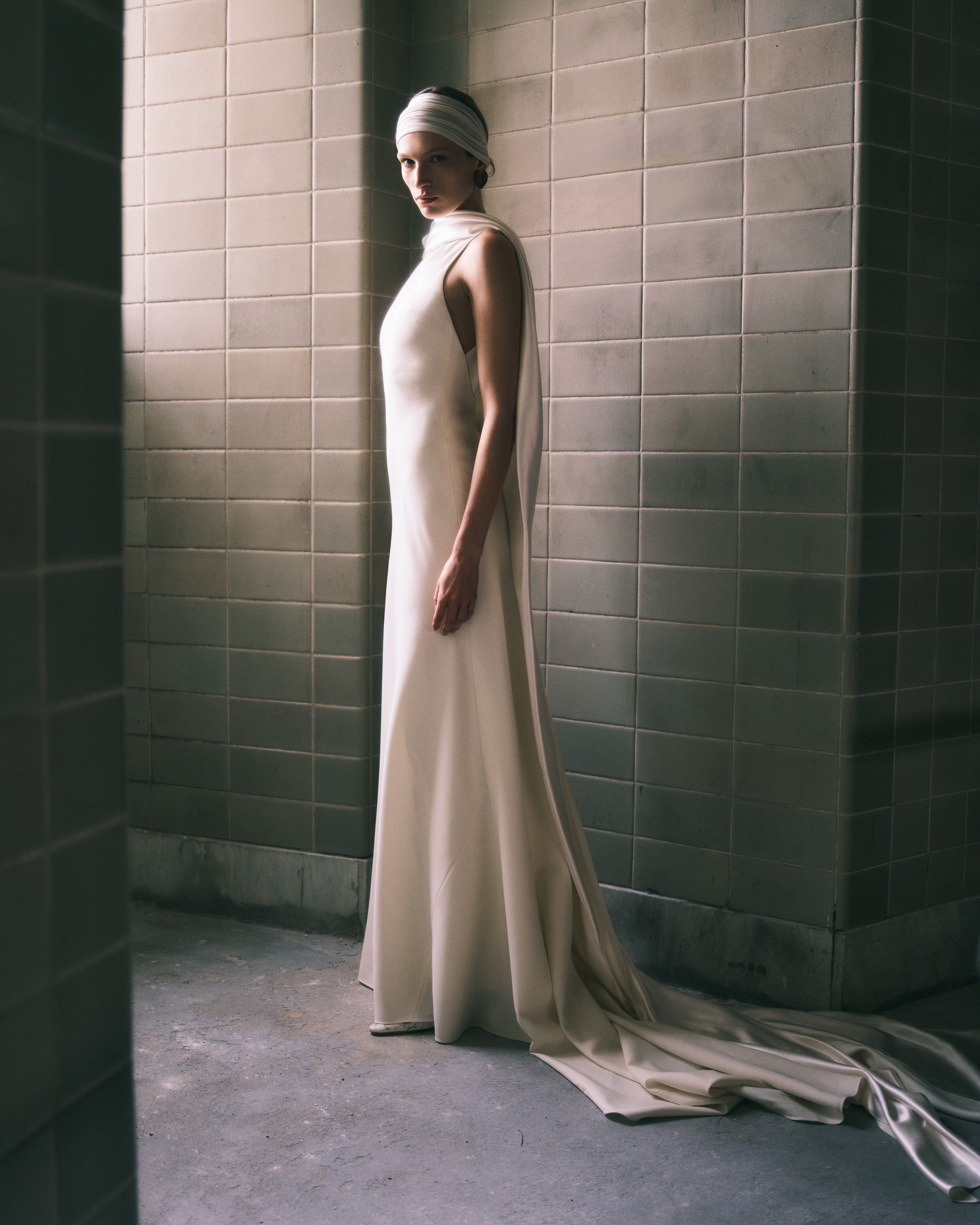Matte wool viscose high neck bias cut gown. Luminous silk wool drapes across the décolletage and falls into an open back, descending into a scarf drape train. Invisible zip closure at center back.