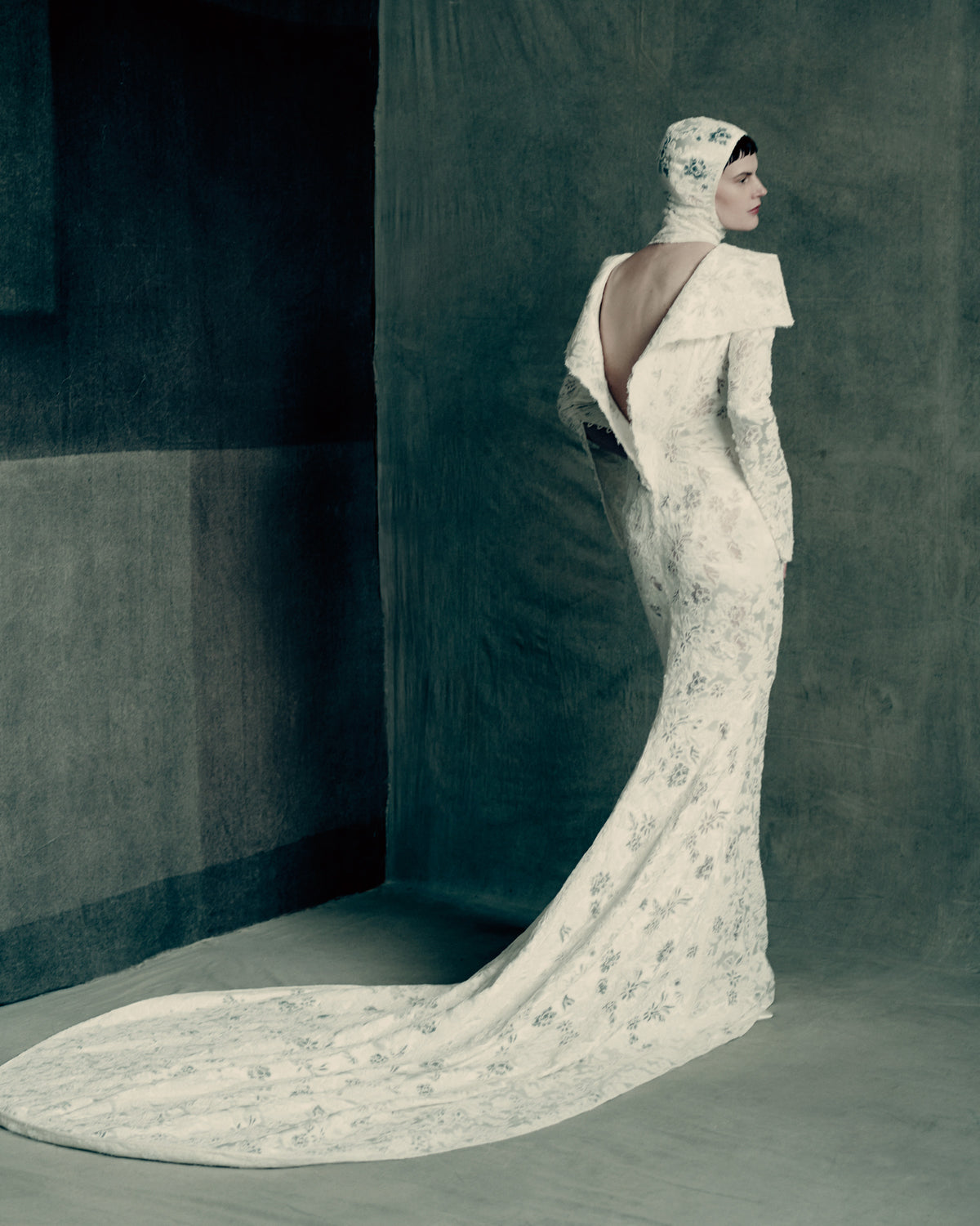 Silk wool gown with corded lace and a sculptural, peeling open back detail. Lustrous silk wool is layered with corded lace, re-embroidered and delicately cut away to create dimensional layers of transparency and shine. Self fabric covered buttons at wrist, invisible zip closure at center back. 