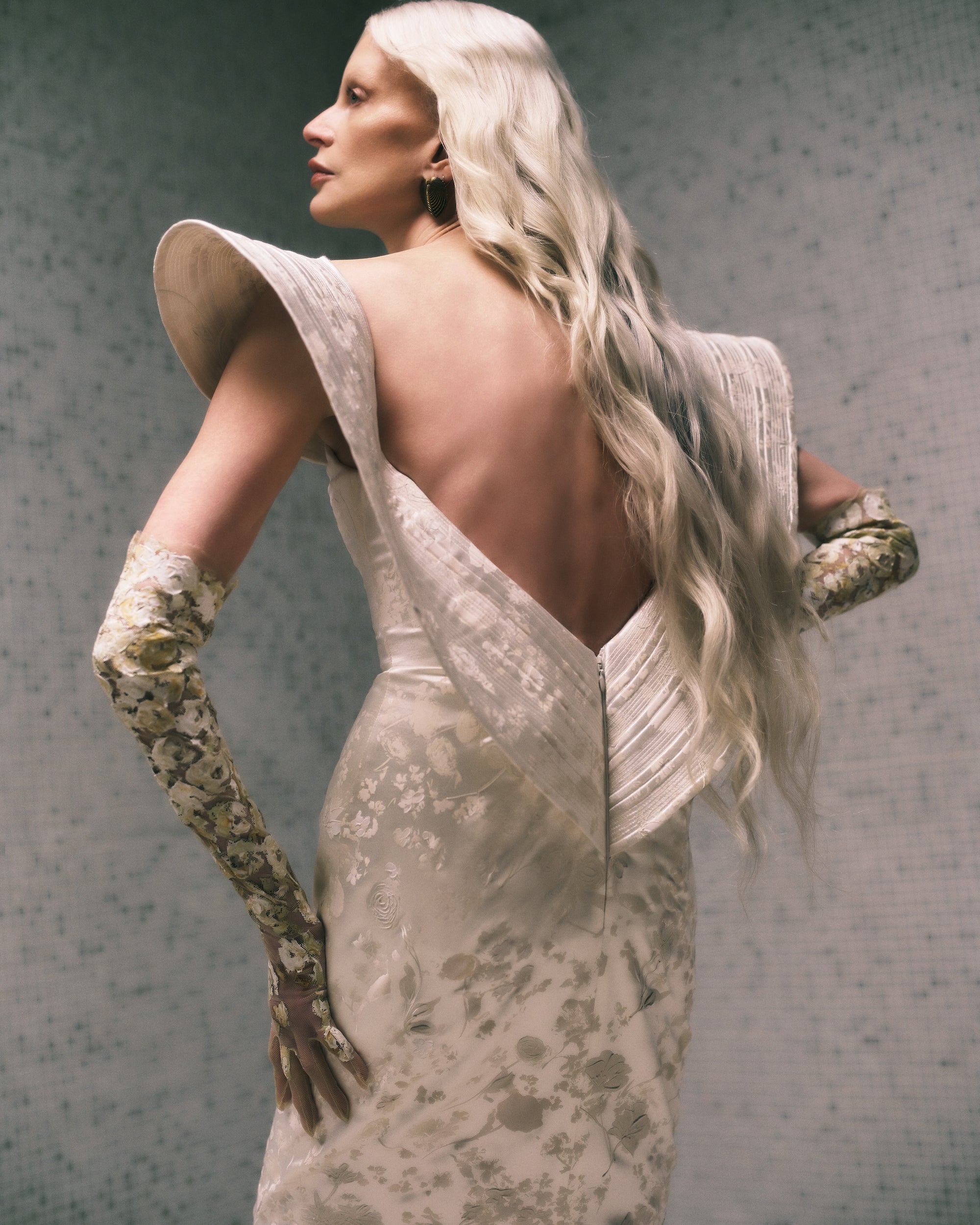 Floral pigment printed and hand painted silk wool column gown. Exaggerated fluted collar drape with trapunto stitch detailing peels from neckline falling down center back. Internal grosgrain belt and invisible zip closure at center back.