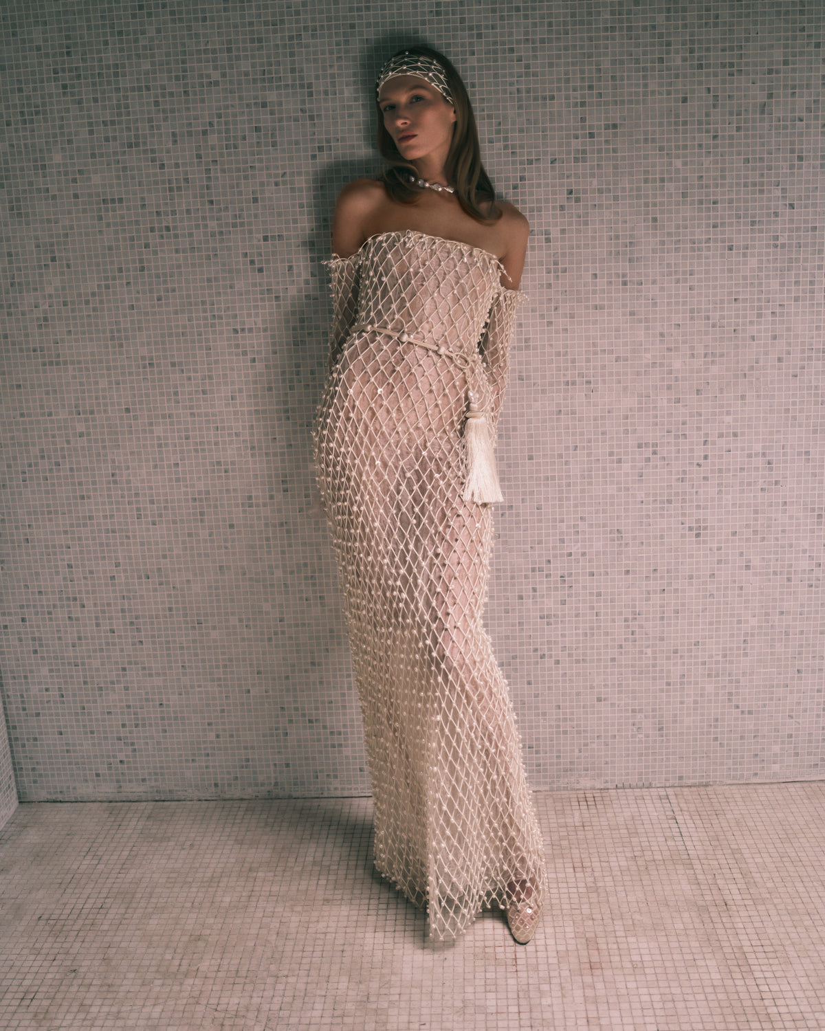 Warped transparent organza off the shoulder column gown with hand applied corded trellis embroidery embellished in transparent sequins and baroque pearls. Fringe hem detail at sleeves is finished with genuine teardrop pearls. Bobinette lining with boned internal bustier. Invisible zip closure at center back.