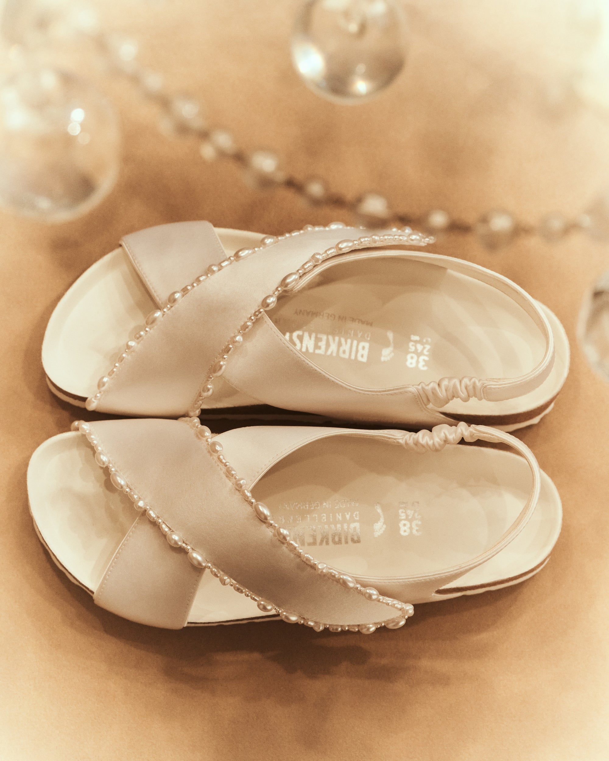 The Tulum is reimagined in a luminous ivory satin, featuring a graceful crossover profile and a slim ankle strap adorned with delicate pearls. The design also introduces an innovative adjustable hidden buckle closure. Handcrafted in Germany, the shoe merges BIRKENSTOCK’s legendary comfort with Danielle Frankel’s signature touch of refined elegance.- Upper: Delicate satin upper, naturally shaped pearls handstitched on trim- Footbed: Anatomical shaped BIRKENSTOCK cork latex Footbed lined with premium Nappa Leather- Sole: EVA die cut outsole with a custom design, blending classic BIRKENSTOCK bone pattern with delicate leaf inspired detailing