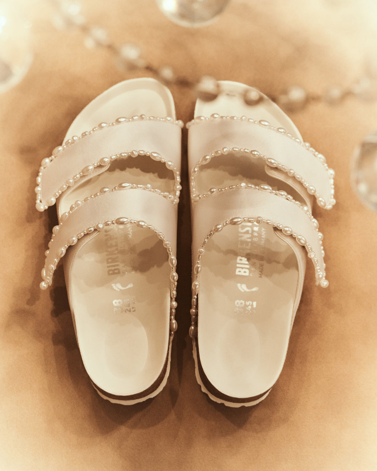 The Arizona is elevated in luminous ivory satin with piped trim detail, accented with delicate pearl edging for a refined and ceremonial finish. The design also introduces an innovative adjustable hidden buckle closure. Handcrafted in Germany, the shoe blends BIRKENSTOCK’s iconic comfort with Danielle Frankel’s bridal elegance.- Upper: Delicate satin upper material- Footbed: Anatomical shaped BIRKENSTOCK cork latex Footbed lined with premium Nappa Leather- Sole: EVA die cut outsole with a custom design, blending classic BIRKENSTOCK bone pattern with delicate lace inspired detailing