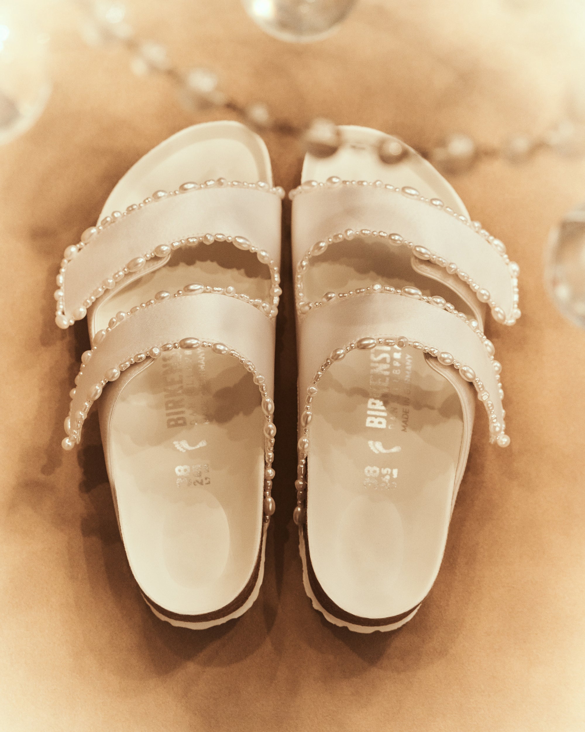 The Arizona is elevated in luminous ivory satin with piped trim detail, accented with delicate pearl edging for a refined and ceremonial finish. The design also introduces an innovative adjustable hidden buckle closure. Handcrafted in Germany, the shoe blends BIRKENSTOCK’s iconic comfort with Danielle Frankel’s bridal elegance.- Upper: Delicate satin upper material- Footbed: Anatomical shaped BIRKENSTOCK cork latex Footbed lined with premium Nappa Leather- Sole: EVA die cut outsole with a custom design, blending classic BIRKENSTOCK bone pattern with delicate lace inspired detailing