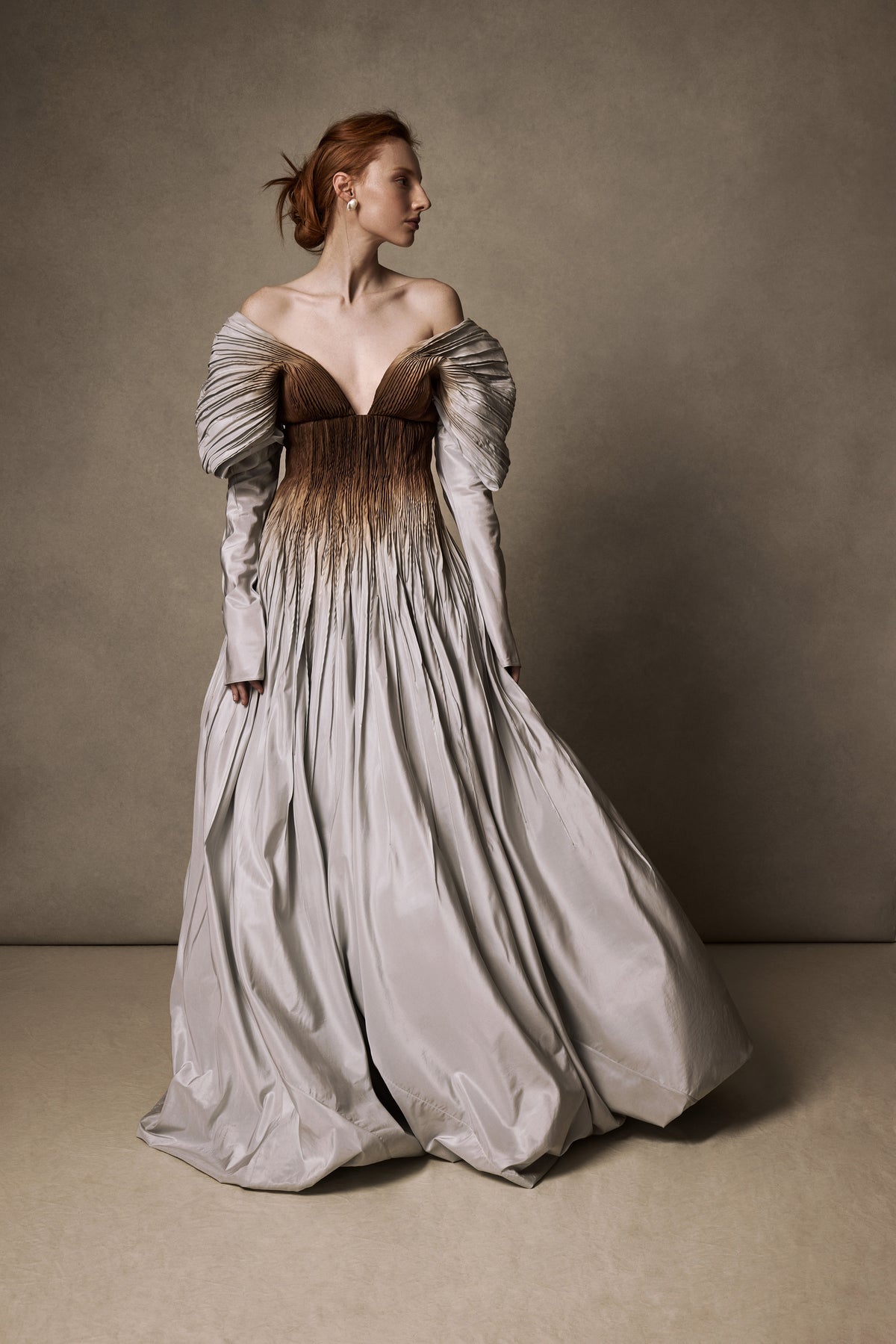 Tucked taffeta off the shoulder ball gown with crinoline encapsulated bubble hem. Boning and gummy tape at neckline for structure and security leading into draped, full length sleeves. Soft internal corset with wireless cups, grosgrain waistband with 3 position closure for support and external center back zipper. Organza and can can lined skirt for volume and hold. Available hand-dyed as editorial version $14990
