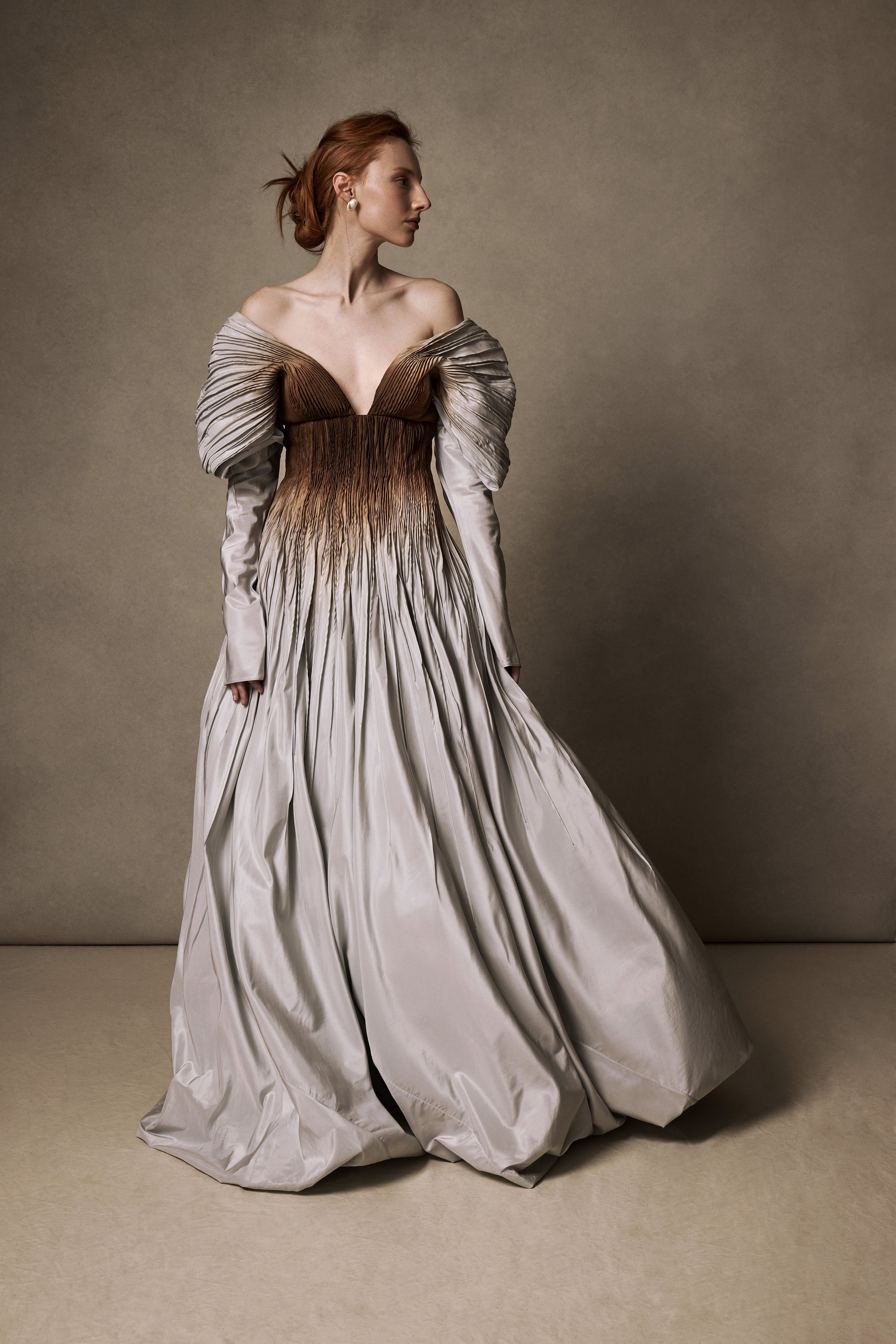 Tucked taffeta off the shoulder ball gown with crinoline encapsulated bubble hem. Boning and gummy tape at neckline for structure and security leading into draped, full length sleeves. Soft internal corset with wireless cups, grosgrain waistband with 3 position closure for support and external center back zipper. Organza and can can lined skirt for volume and hold. Available hand-dyed as editorial version $14990