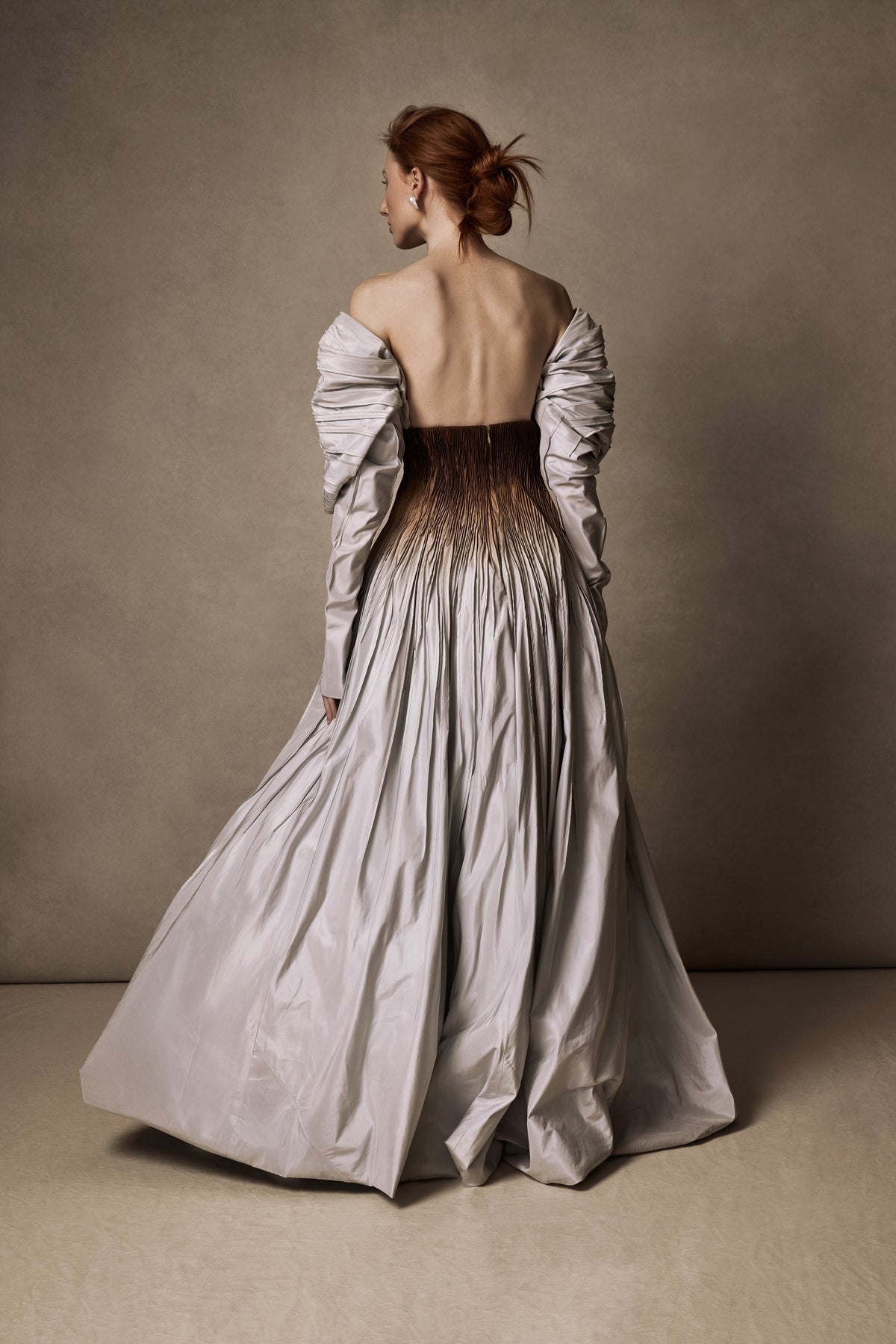 Tucked taffeta off the shoulder ball gown with crinoline encapsulated bubble hem. Boning and gummy tape at neckline for structure and security leading into draped, full length sleeves. Soft internal corset with wireless cups, grosgrain waistband with 3 position closure for support and external center back zipper. Organza and can can lined skirt for volume and hold. Available hand-dyed as editorial version $14990