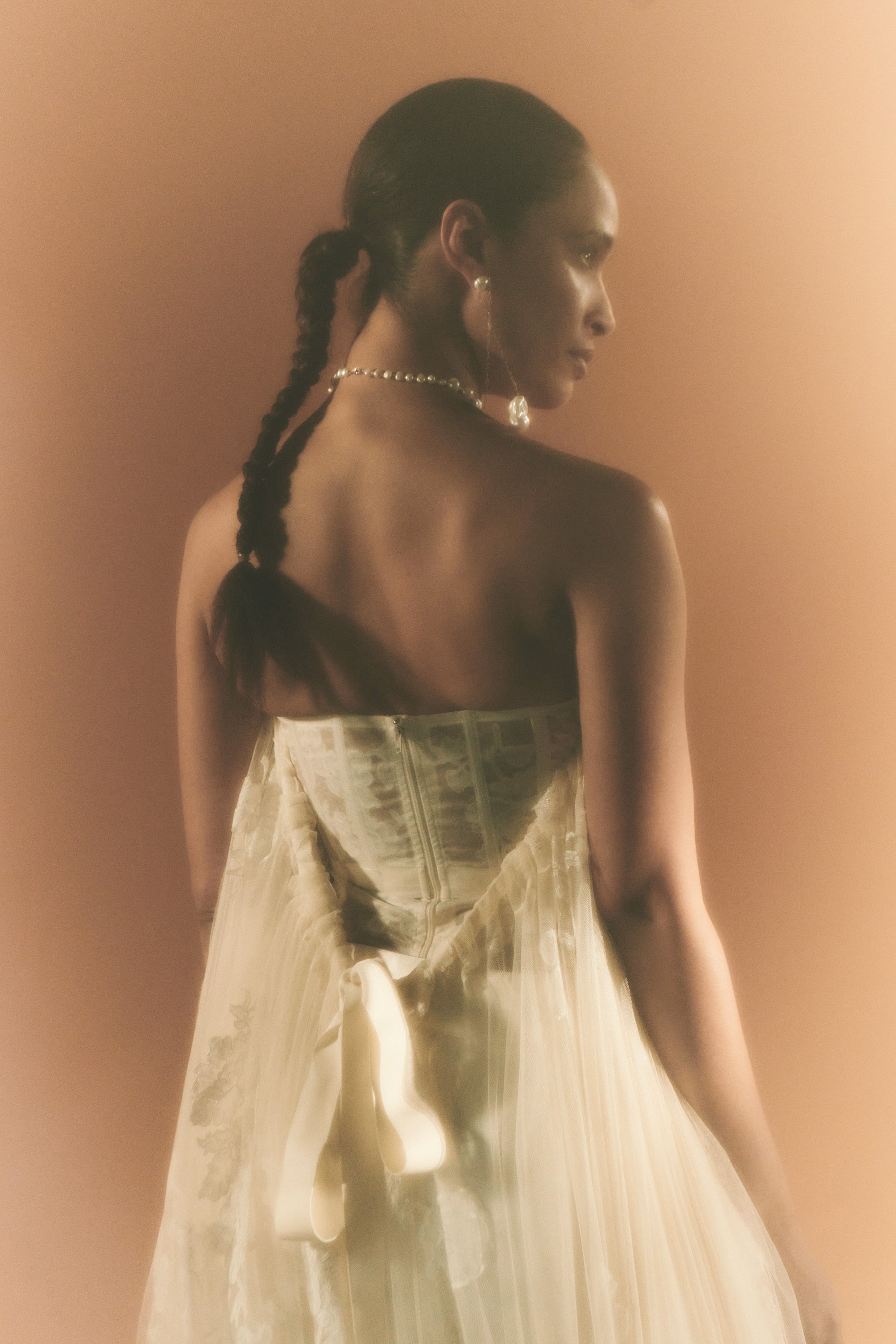 Soft tulle strapless corset top with sheer floral organza back. Hand appliquéd and draped through bodice and overflowing down side body. Tulle and lace train tunneled through grosgrain ribbon accent tie at back. Side boning and soft cups for support and center back zip to close.Styled with Miriam pant