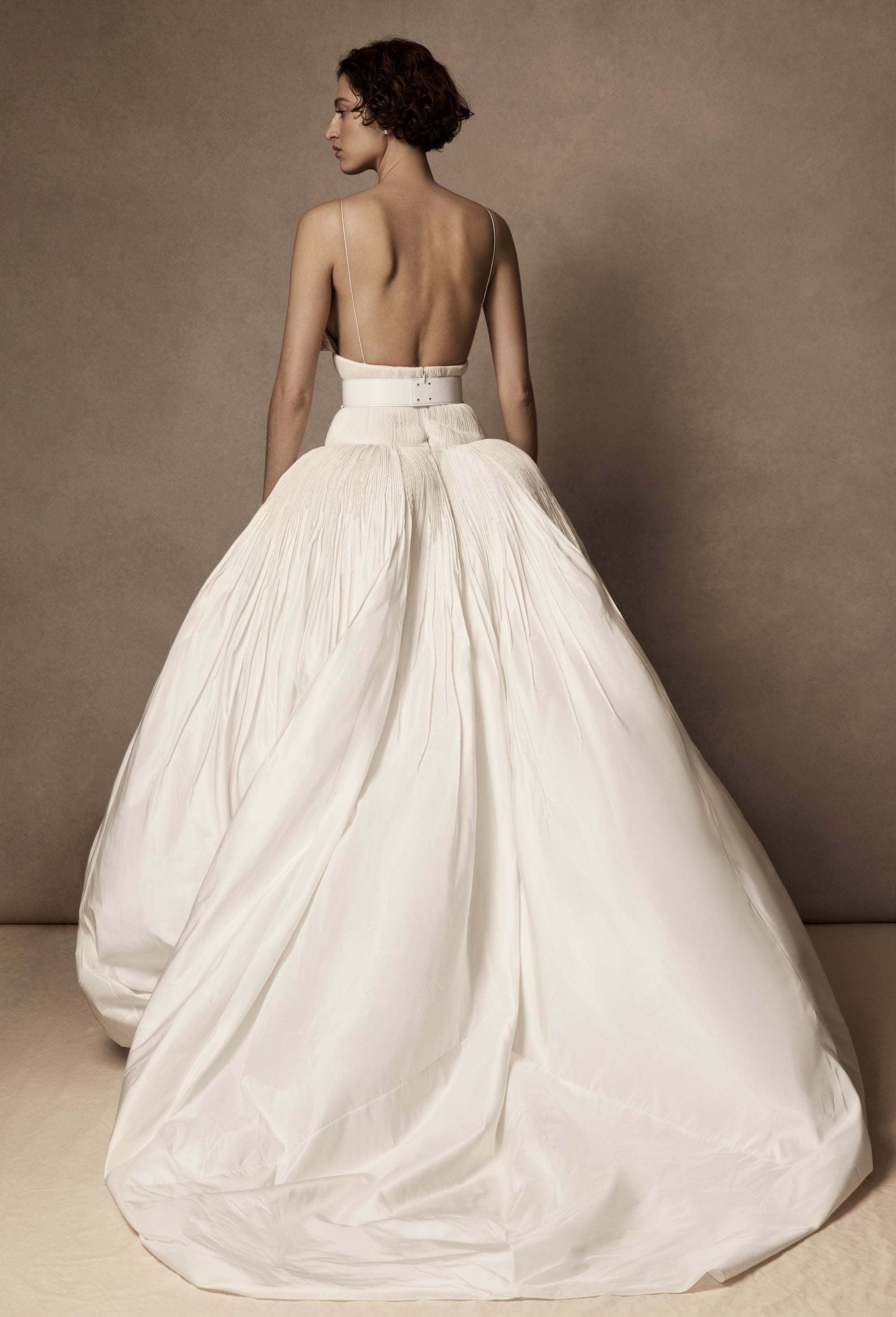 Micro-tucked silk taffeta ballgown. Crinoline enclosed, bubbled skirt with extended train. Soft triangular cups for support beneath abstract triangular draped taffeta panels. Soft boning for structure and center back close. The belt is sold separately.
