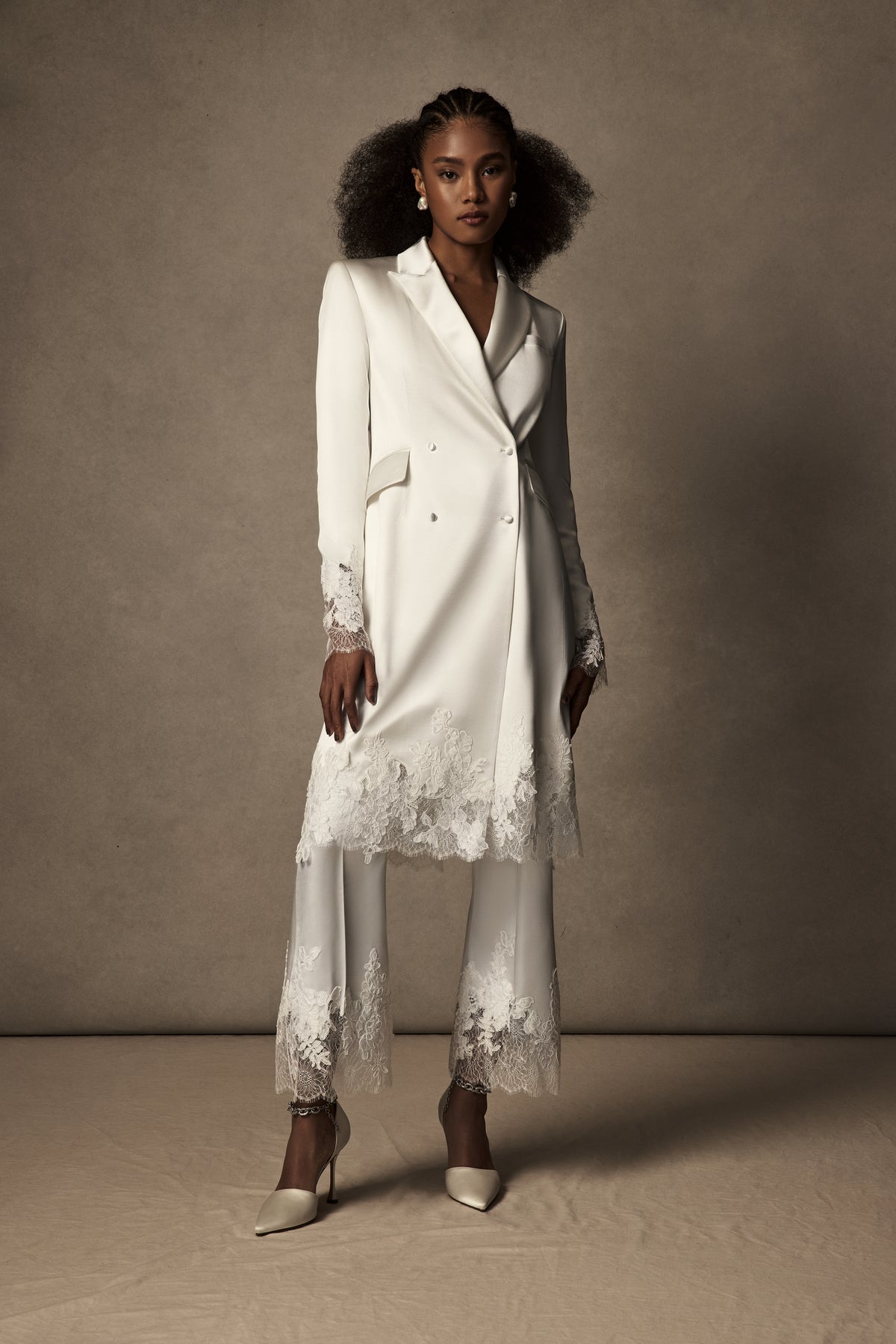 Double breasted lace mended midi overcoat. Silk wool body with peaked lapels and flap pocket accent at hips. Hand cut appliqués ornamented along lace cuffs and hemline. Shoulder pads for structure and button close.