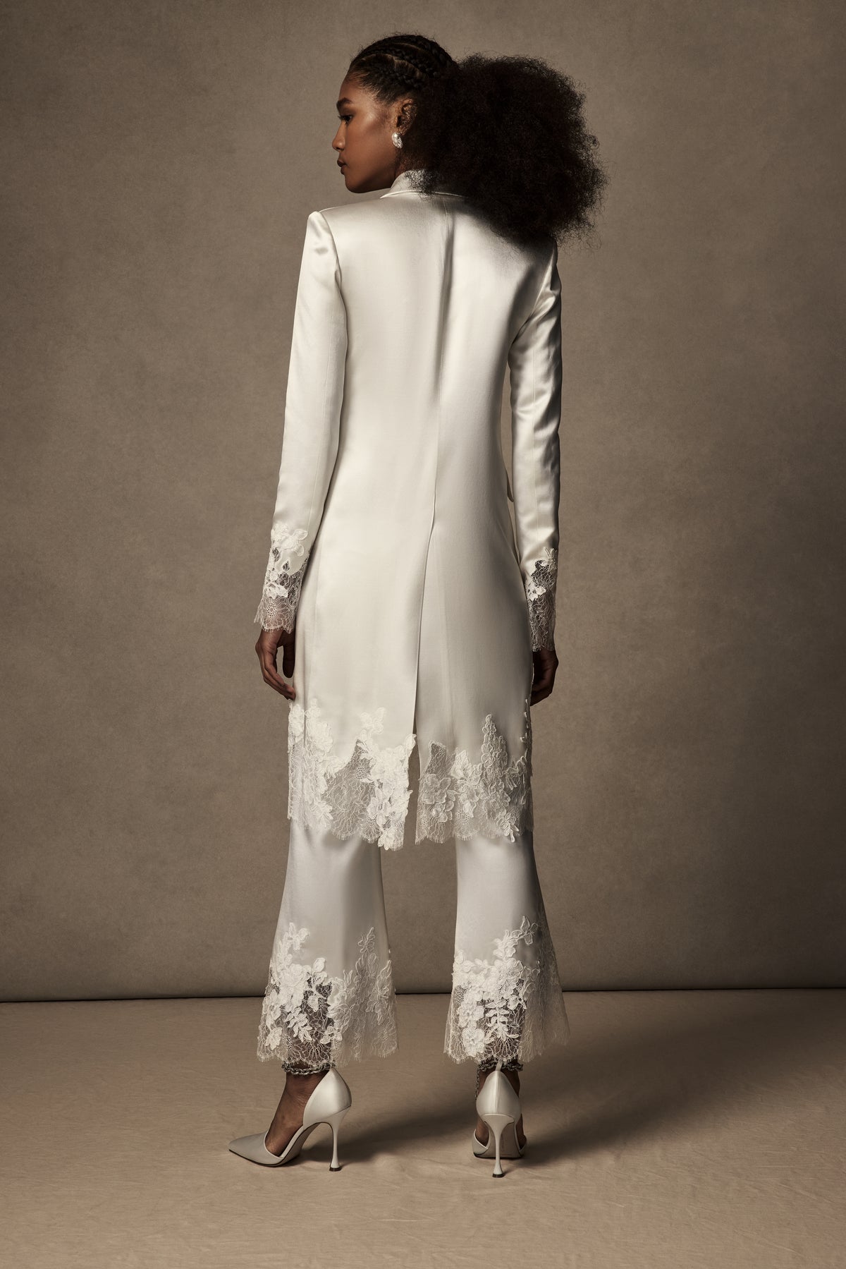 Double breasted lace mended midi overcoat. Silk wool body with peaked lapels and flap pocket accent at hips. Hand cut appliqués ornamented along lace cuffs and hemline. Shoulder pads for structure and button close.