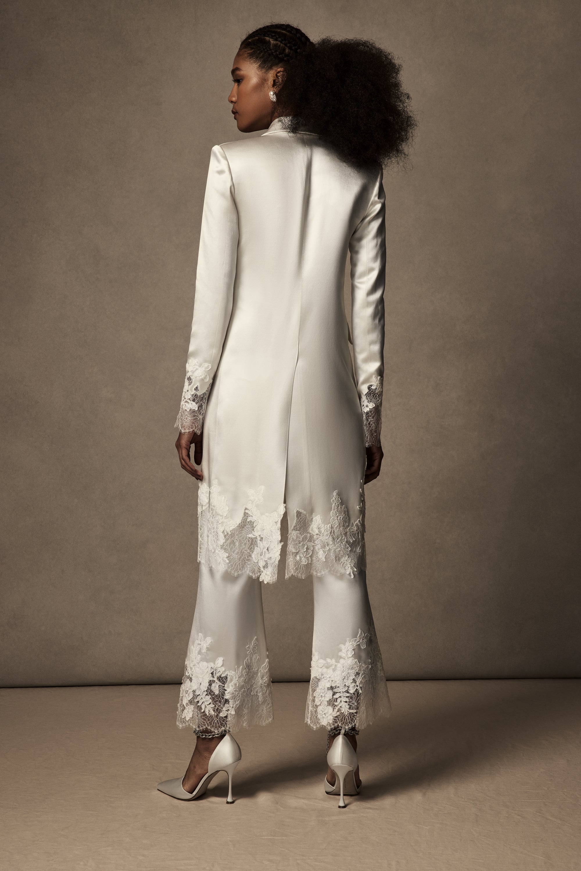 Double breasted lace mended midi overcoat. Silk wool body with peaked lapels and flap pocket accent at hips. Hand cut appliqués ornamented along lace cuffs and hemline. Shoulder pads for structure and button close.
