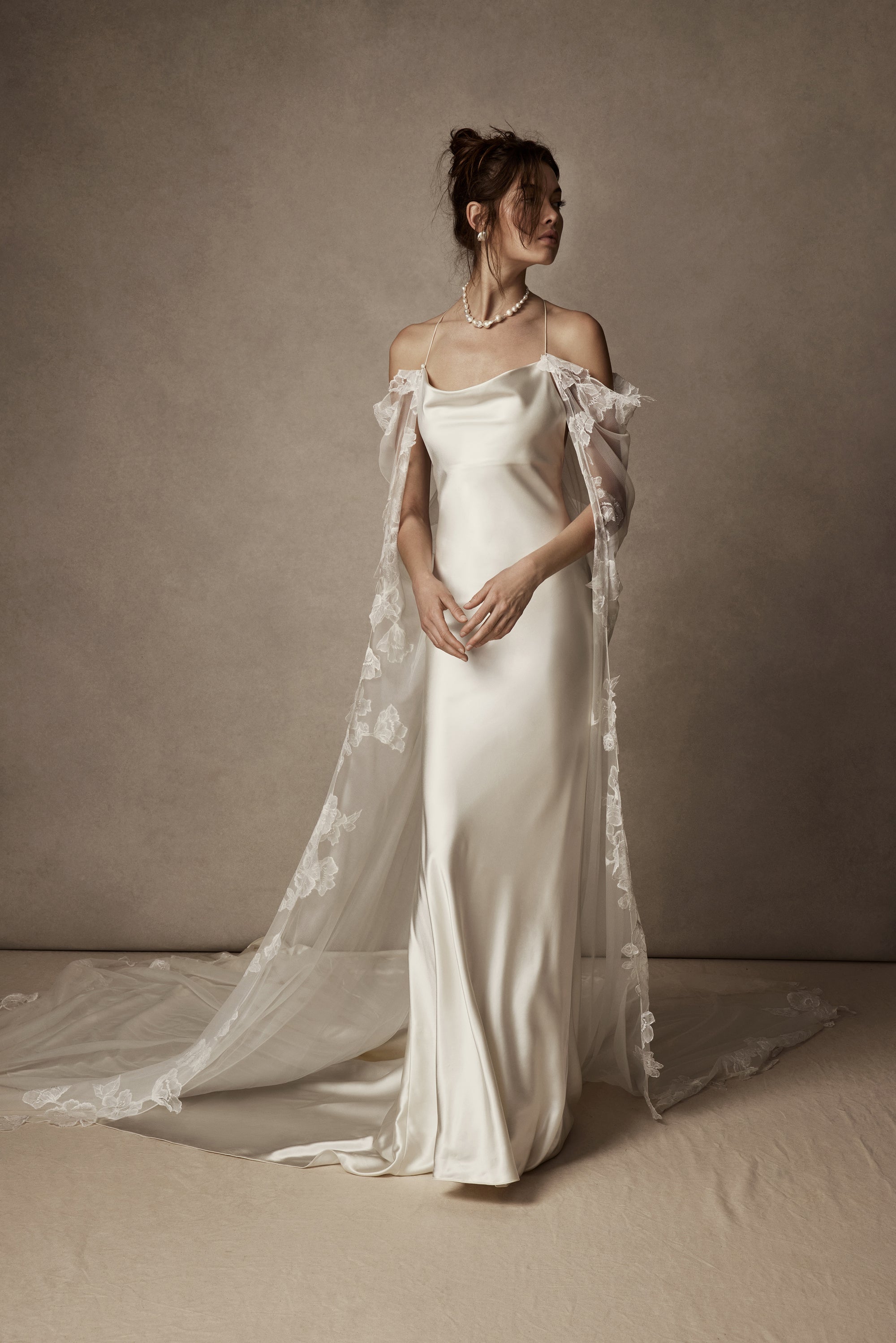 Cowled neck, crepe back satin slip gown. Low scooped back with cross back spaghetti straps. Detachable tulle cape with hand appliquéd chantilly lace edging along sides. Center back zip, hook and eye closure.