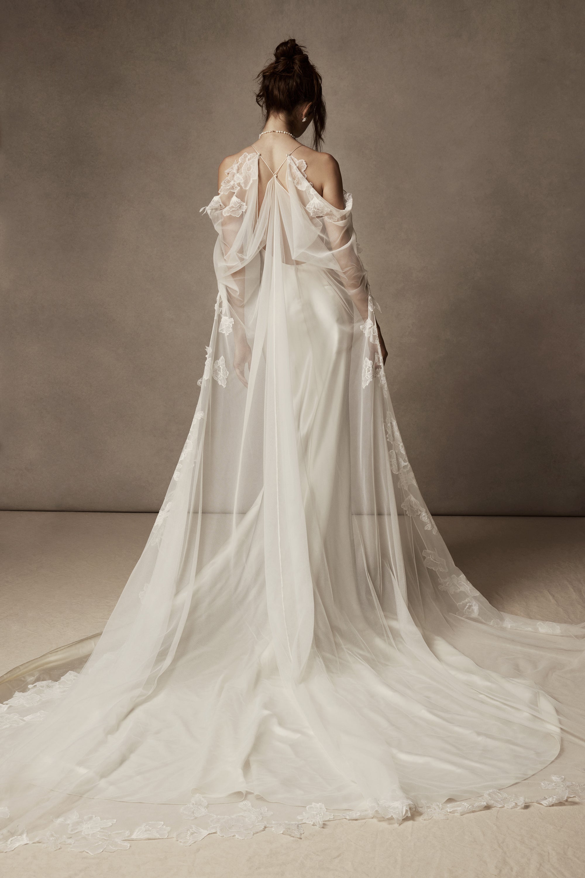 Cowled neck, crepe back satin slip gown. Low scooped back with cross back spaghetti straps. Detachable tulle cape with hand appliquéd chantilly lace edging along sides. Center back zip, hook and eye closure.