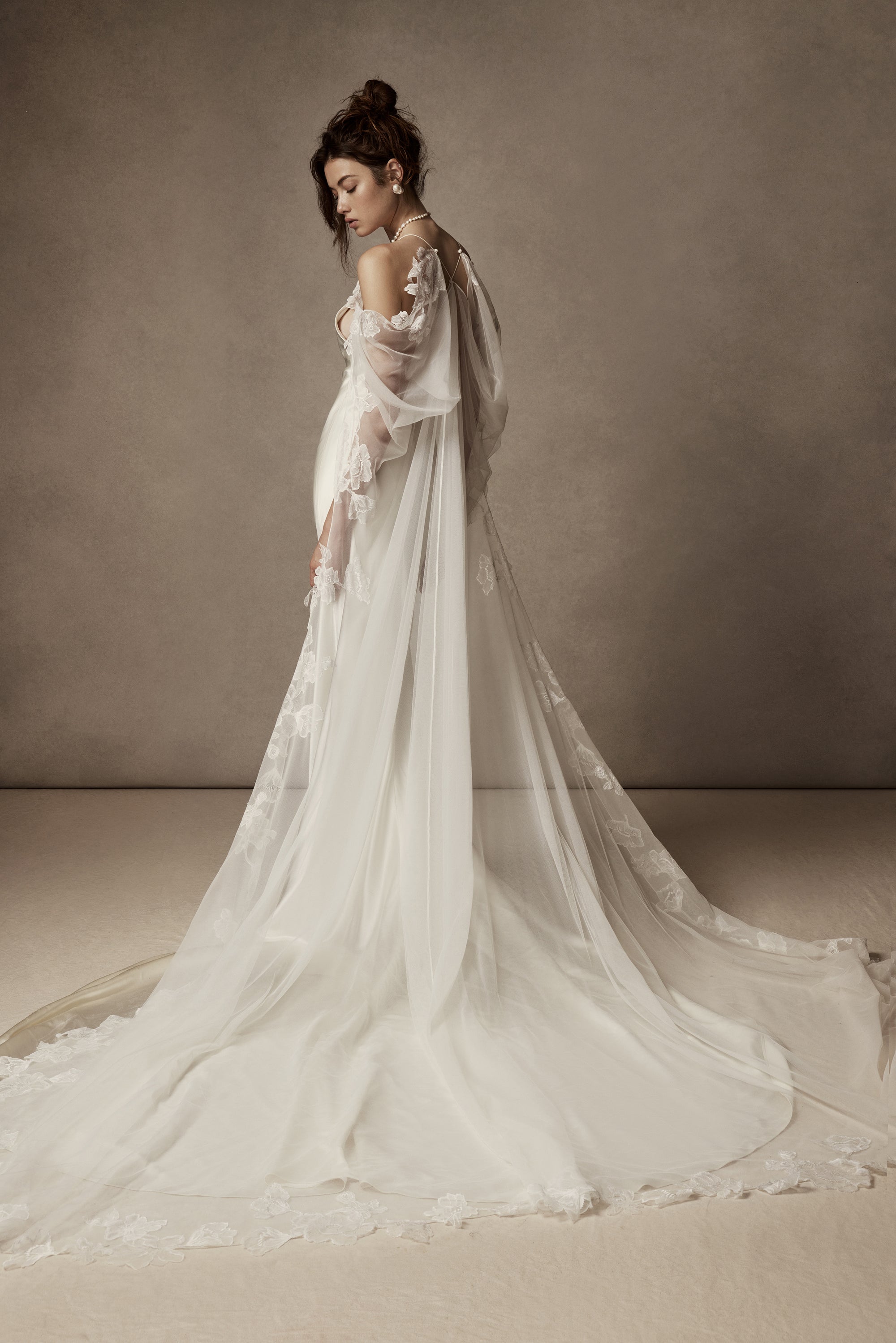 Cowled neck, crepe back satin slip gown. Low scooped back with cross back spaghetti straps. Detachable tulle cape with hand appliquéd chantilly lace edging along sides. Center back zip, hook and eye closure.