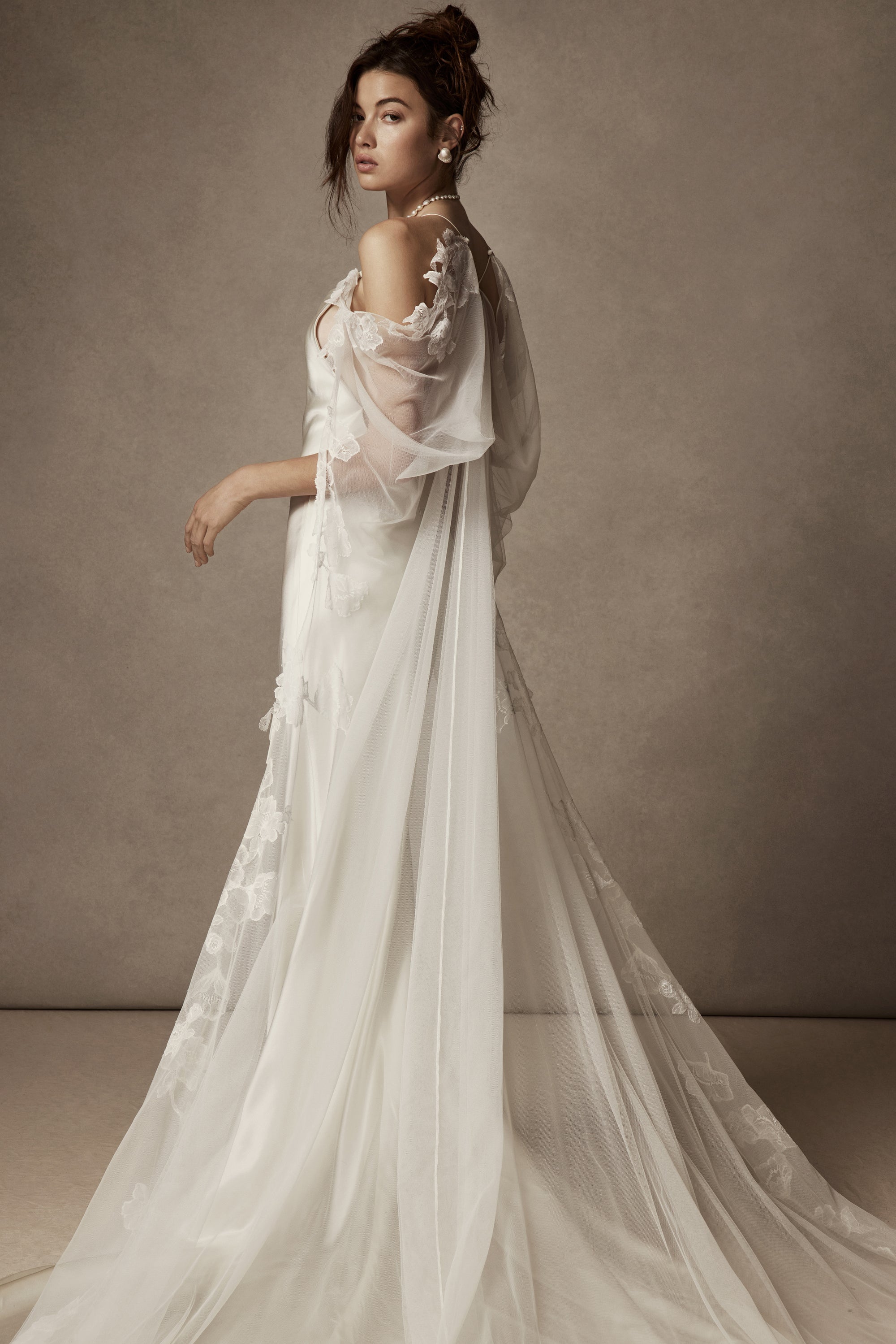 Cowled neck, crepe back satin slip gown. Low scooped back with cross back spaghetti straps. Detachable tulle cape with hand appliquéd chantilly lace edging along sides. Center back zip, hook and eye closure.
