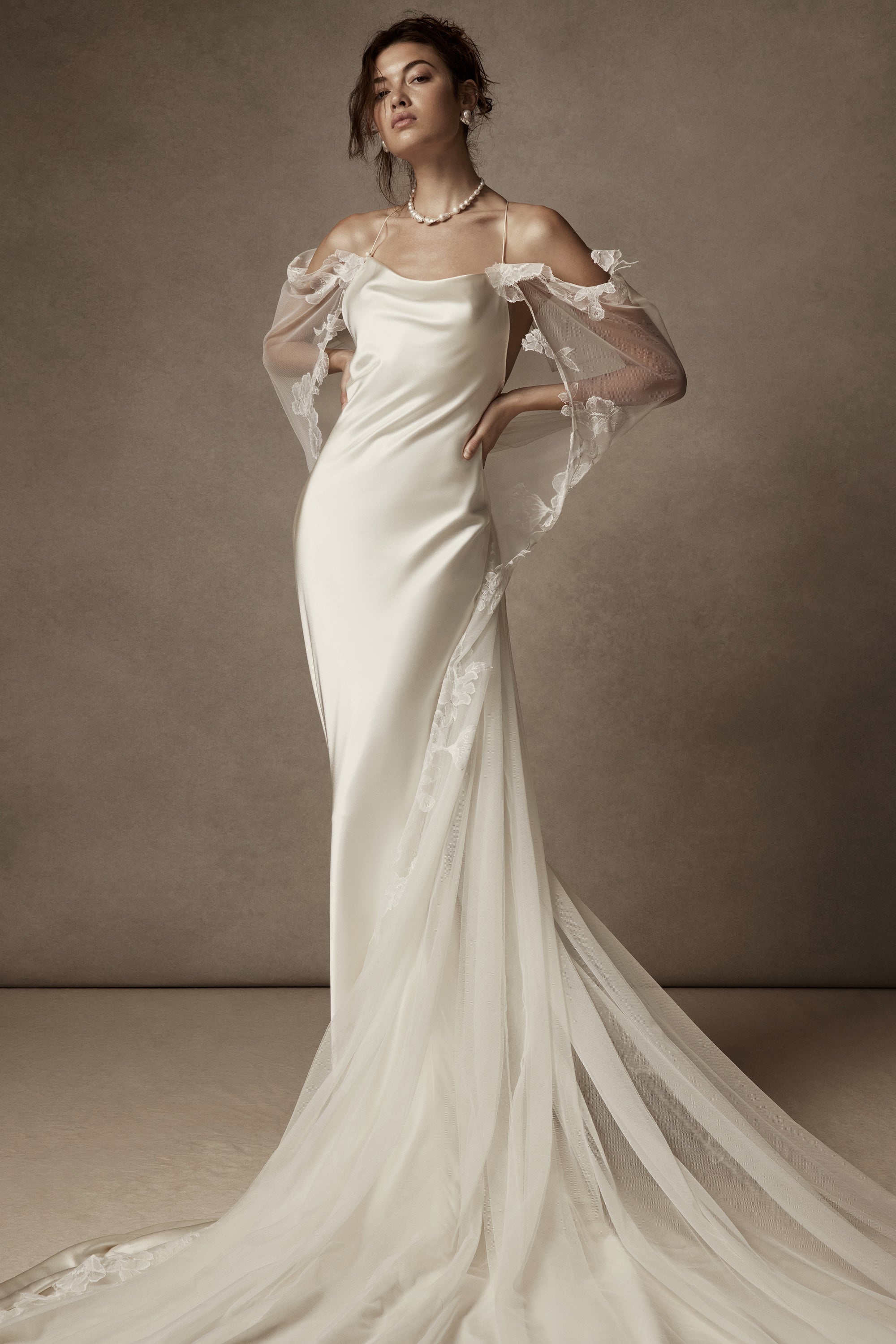 Cowled neck, crepe back satin slip gown. Low scooped back with cross back spaghetti straps. Detachable tulle cape with hand appliquéd chantilly lace edging along sides. Center back zip, hook and eye closure.