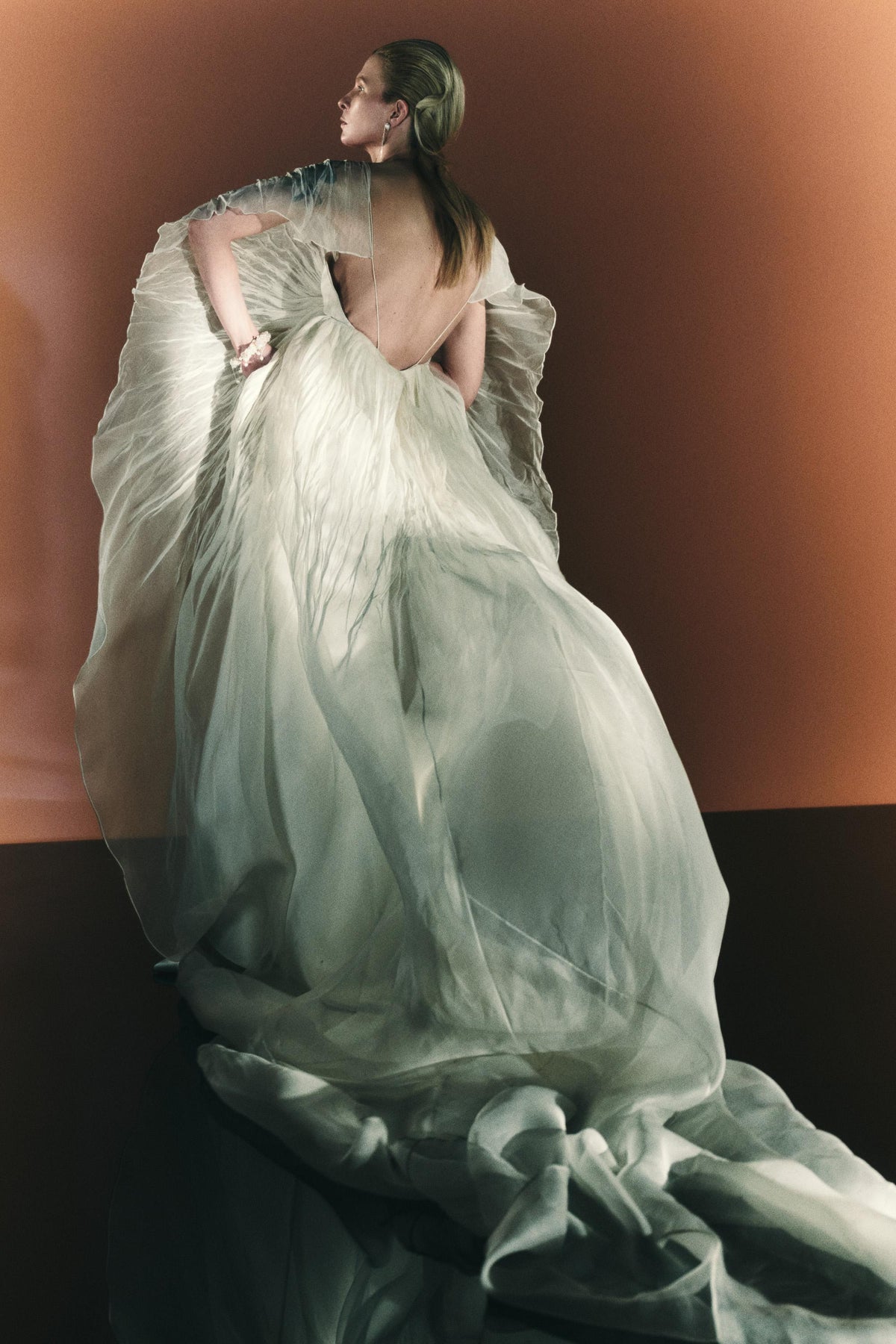 Silk wool and pin-tucked organza cape gown. Billowing, hand pleated organza sleeve releasing from center front of camisole slip gown to spaghetti strap back. Organza pin-tuck bursts along low v-back into extended train. Soft body construction and center back close.