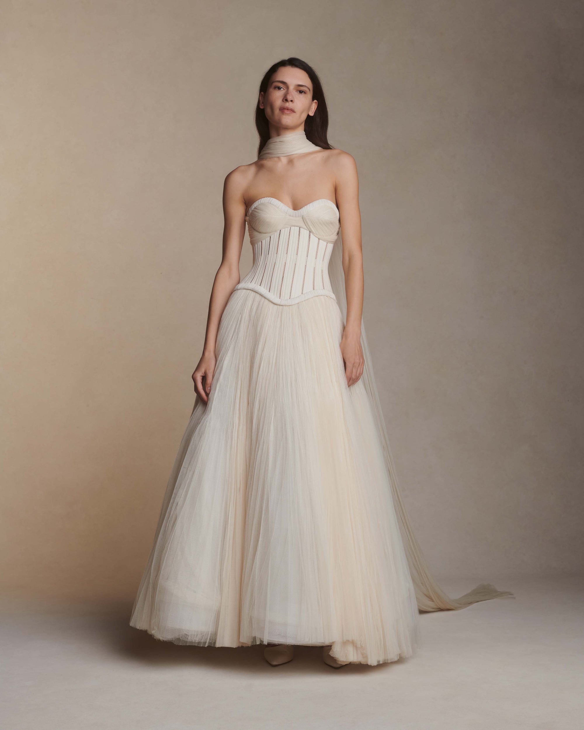 Tulle and twill corseted tea length ball gown. Lace and piped cotton twill bodice with full hook and eye back closure. Exaggerated soft tulle, pleated panels at bust to drape over the body. Sunburst pleated, hand crinkled tulle skirt upon silk organza base. Crinoline for structure and center back zip to close.