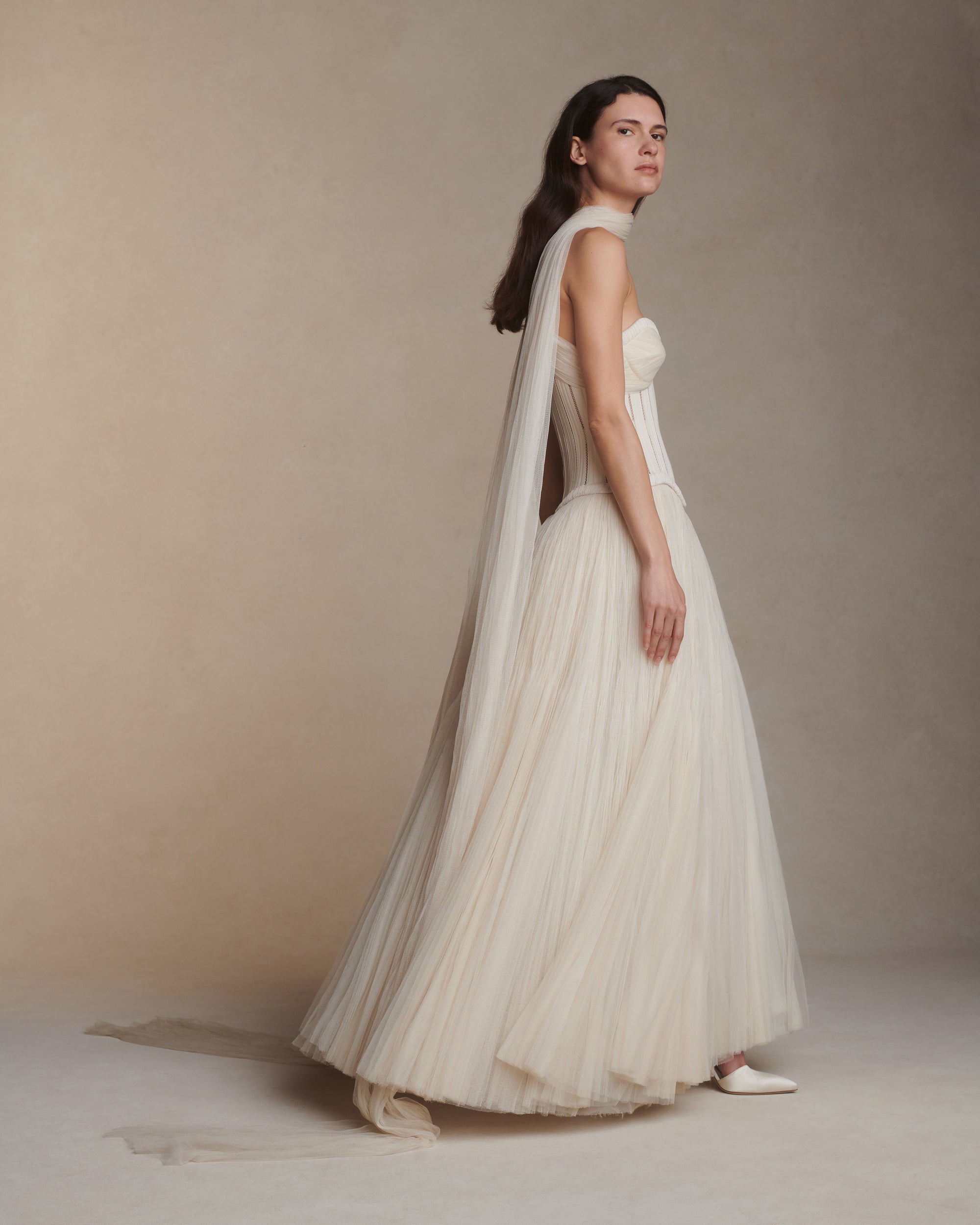 Tulle and twill corseted tea length ball gown. Lace and piped cotton twill bodice with full hook and eye back closure. Exaggerated soft tulle, pleated panels at bust to drape over the body. Sunburst pleated, hand crinkled tulle skirt upon silk organza base. Crinoline for structure and center back zip to close.