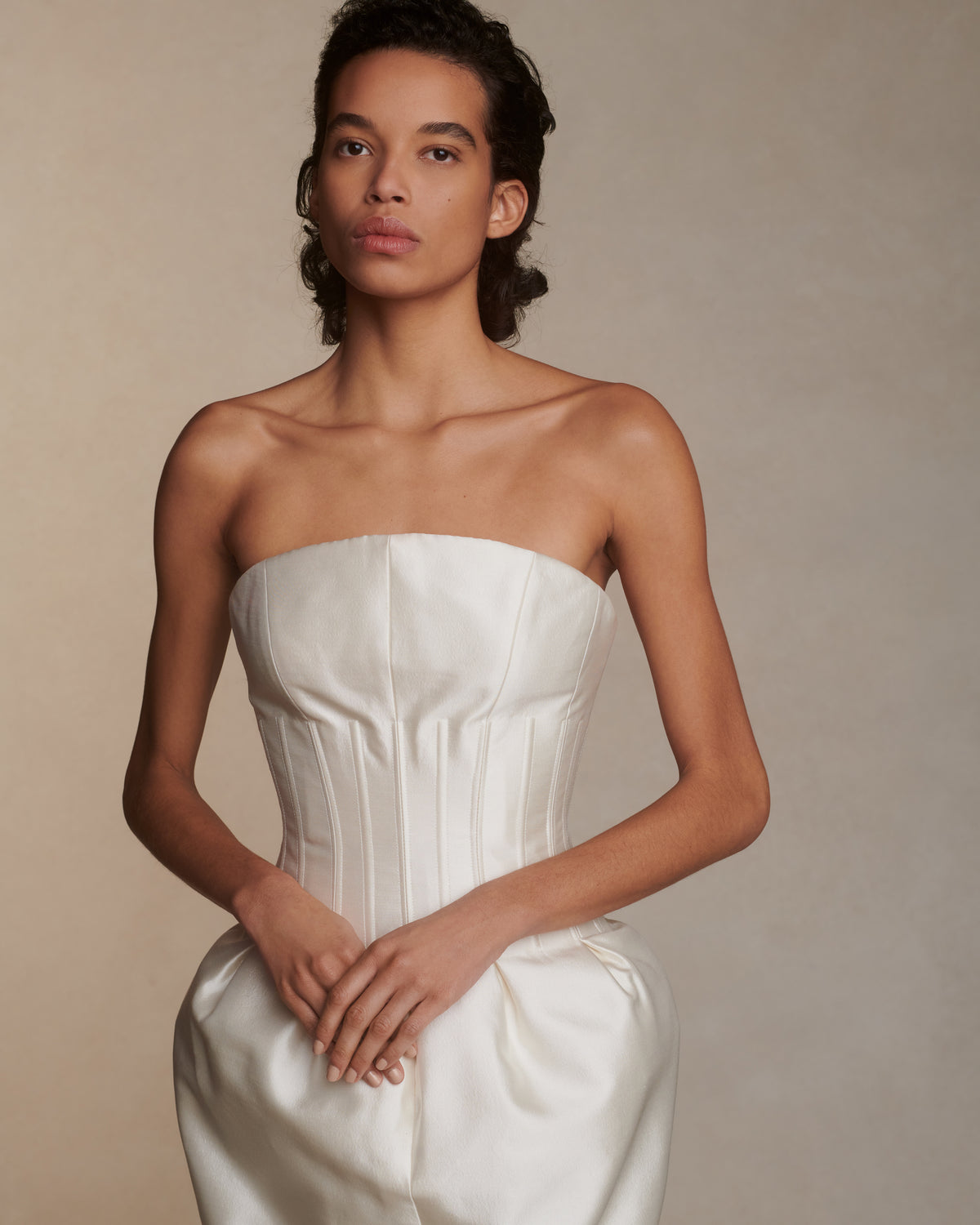 Luminous silk wool twill tea length gown. Boned waist with sculptural inverted pleats extends into a structured bust with curved neckline. Side seam pockets, soft cups, internal grosgrain waistband, and center back zip closure.