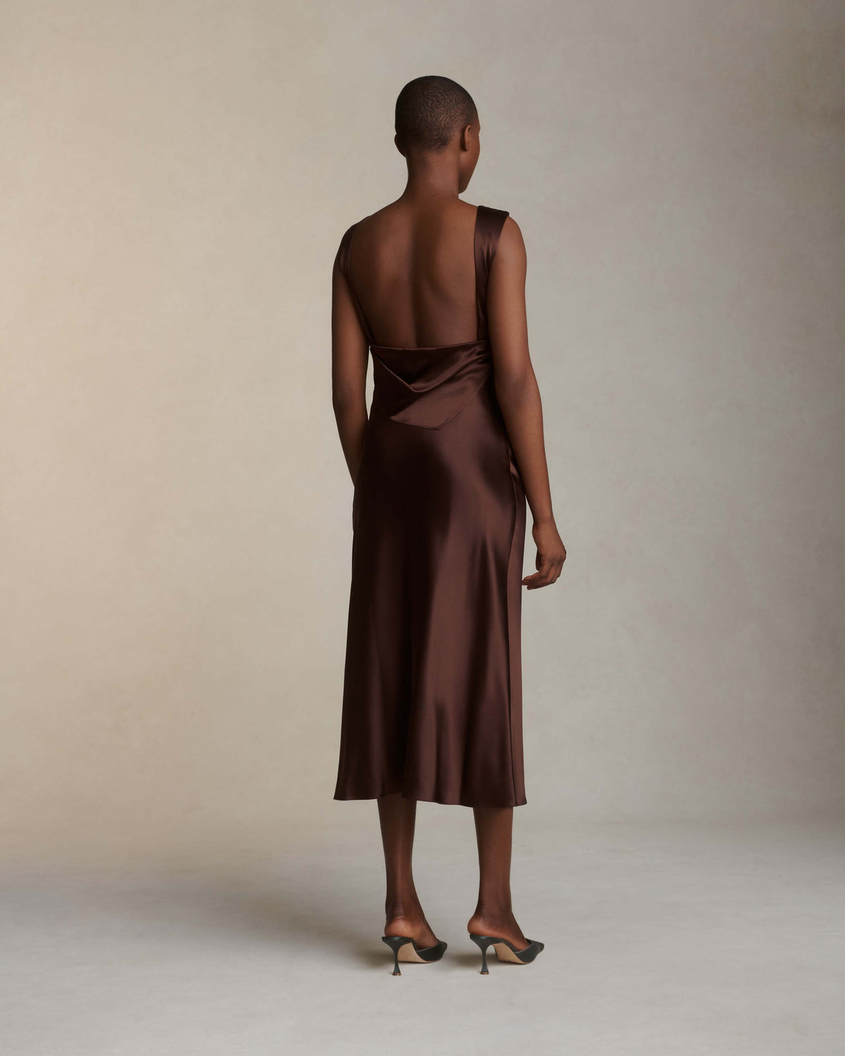 Raised cowl neck, bias cut silk satin sleeveless gown. Open back with scarf draped accent. Fully lined with side zip closure. Midi length.