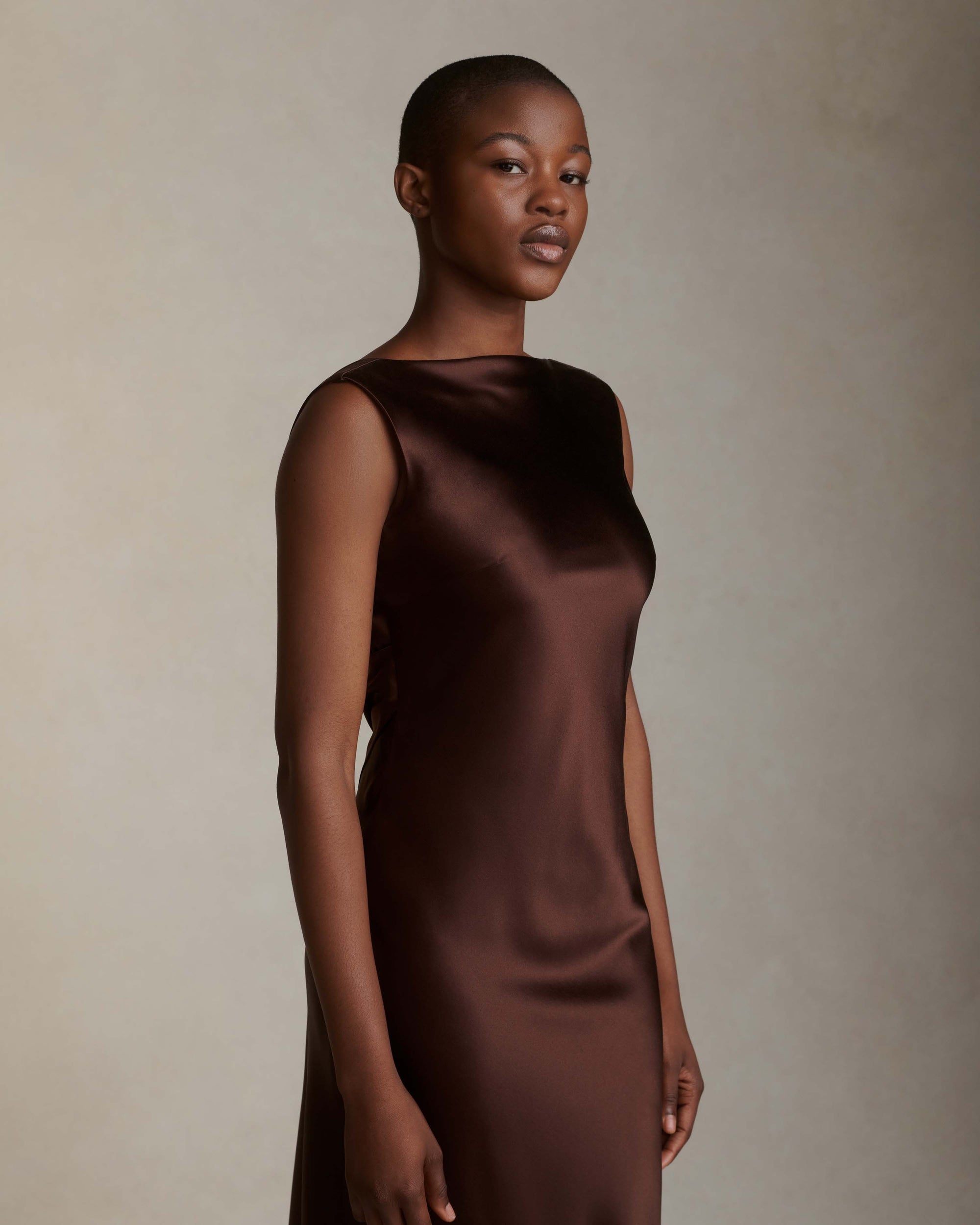 Raised cowl neck, bias cut silk satin sleeveless gown. Open back with scarf draped accent. Fully lined with side zip closure. Midi length.