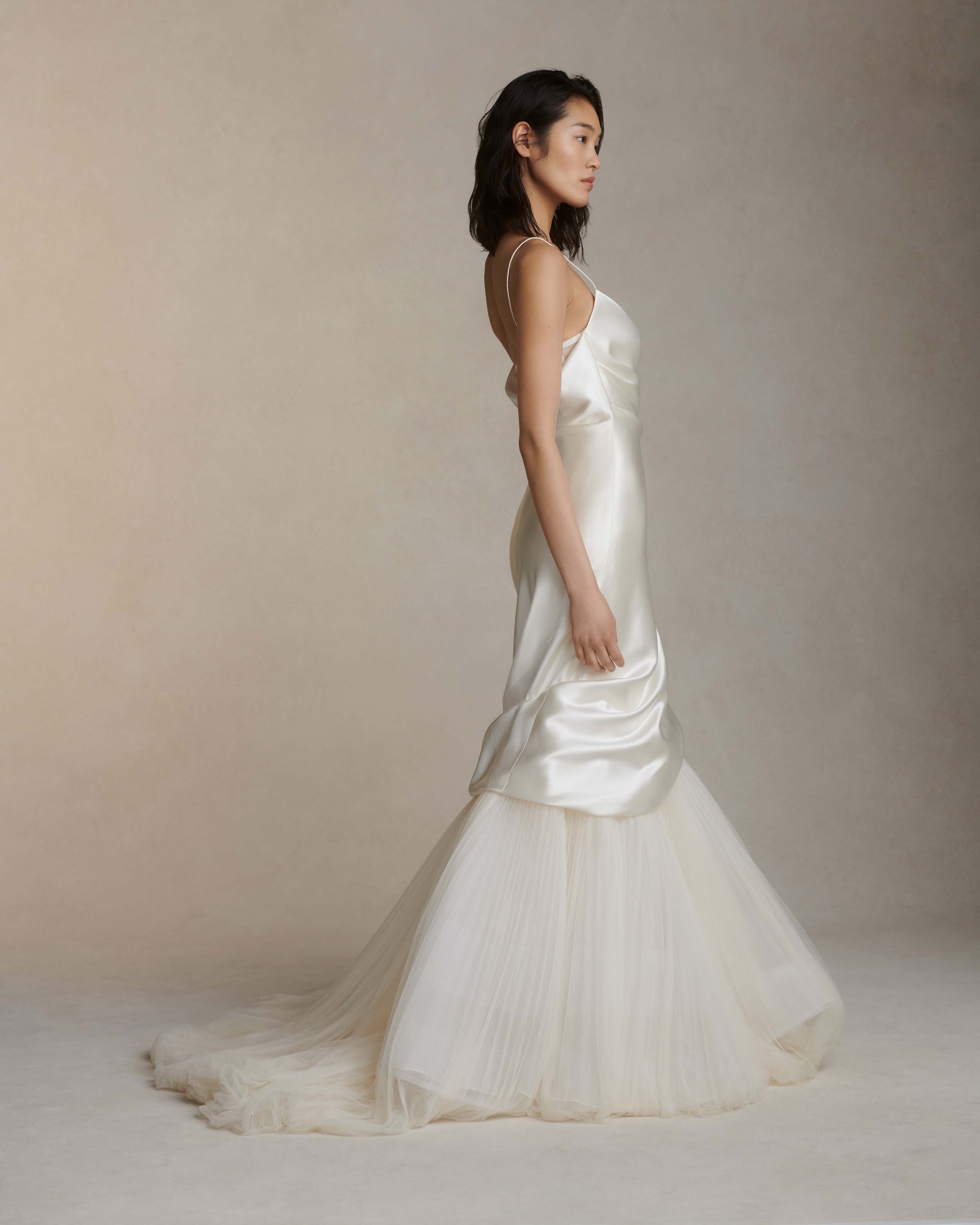 Layered silk wool and soft tulle gown. Fluid draping spills over sunburst pleated tulle skirt with bubble hem. Dipped drape reveals delicate gathered tulle at front neckline and boned organza bustier at back. Soft cups, internal grosgrain waist belt and invisible side zip closure.