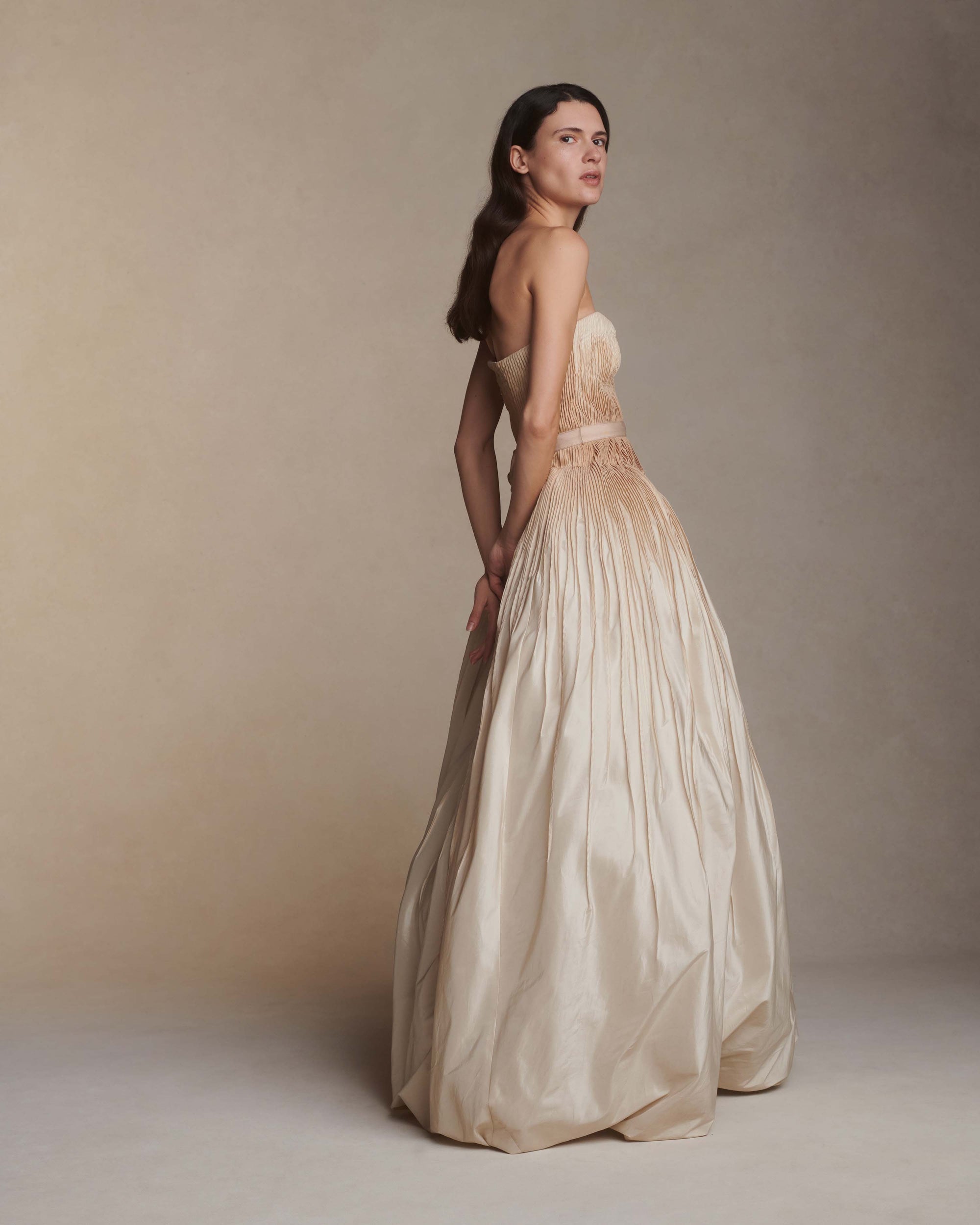 Hand tucked silk taffeta gown with dipped neckline. Micro tucked drop waist bodice with grosgrain waist tie releases into a dramatic skirt with bubbled hem. Hand-dyed ombre bodice fades from under bust and into skirt. Soft internal cups, boning, internal waist belt, invisible center back zip. Available in Ivory $10,990.