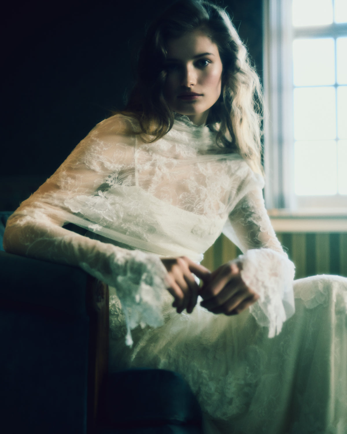 Romantic long sleeve iris lace and soft tulle gown adorned with hand cut chantilly and corded lace appliqués. A diaphanous overlay extends beyond a stretch Cady spaghetti strap foundation into delicate draping across neck and decolletage, spilling into a scarf drape detail at low back. Boned internal bustier, internal grosgrain waist belt and center back zip closure.