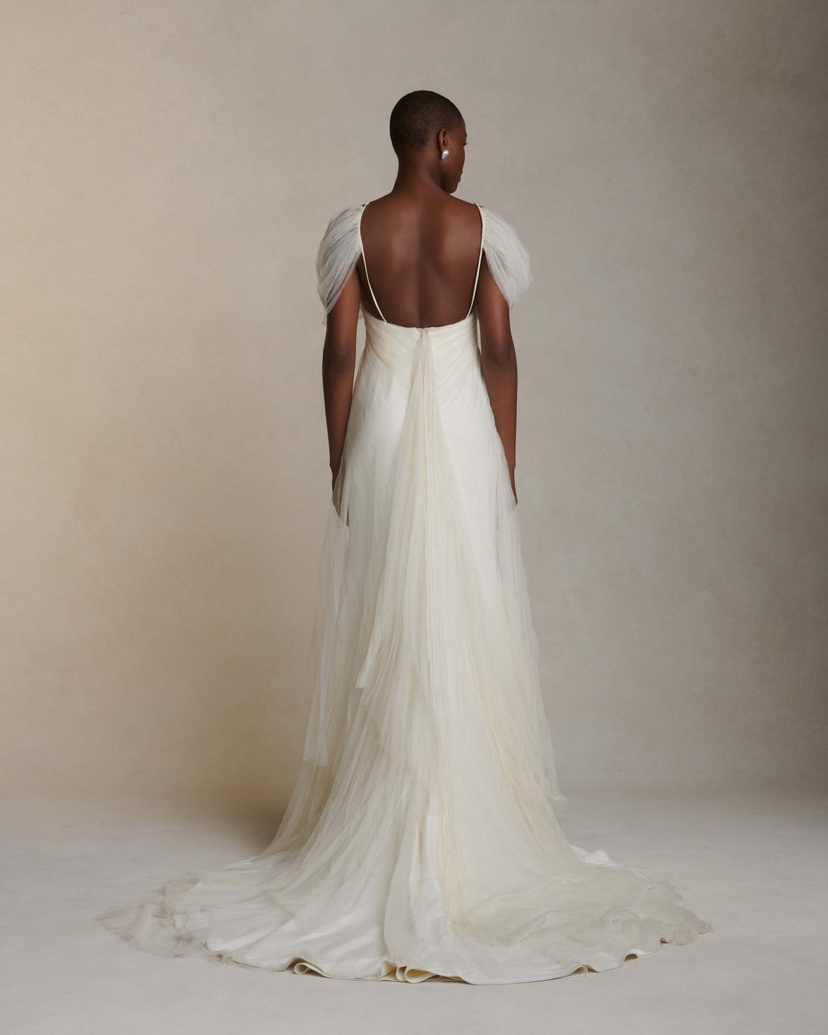 Pleated tulle swagged gown. Off the shoulder soft drapes releasing from center neckline to spaghetti strap back. Sunburst pleated, hand crinkled soft tulle through body and extending down center back for shape and movement. Soft internal bustier with side boning. Low center back zip, hook and eye closure.