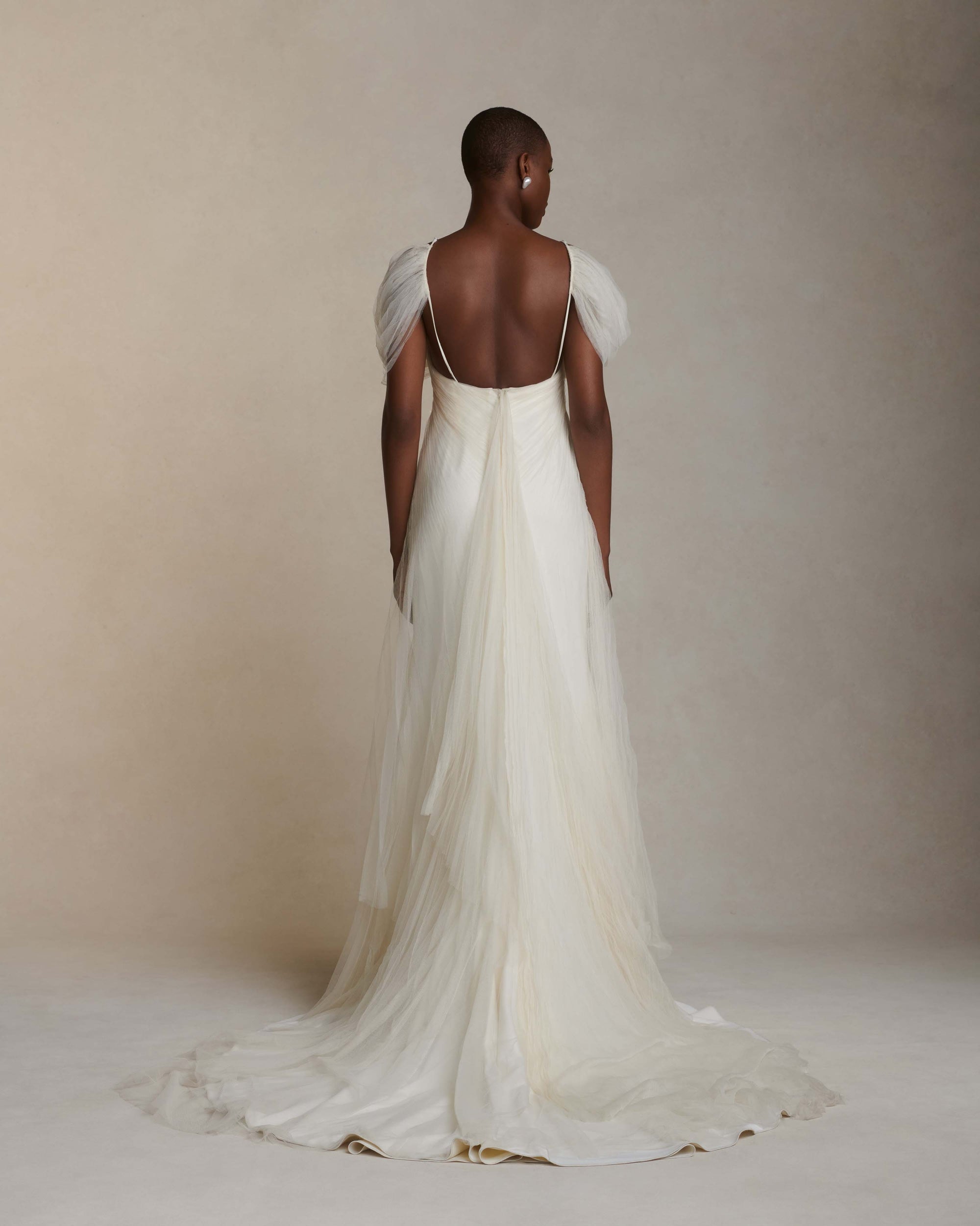 Pleated tulle swagged gown. Off the shoulder soft drapes releasing from center neckline to spaghetti strap back. Sunburst pleated, hand crinkled soft tulle through body and extending down center back for shape and movement. Soft internal bustier with side boning. Low center back zip, hook and eye closure.