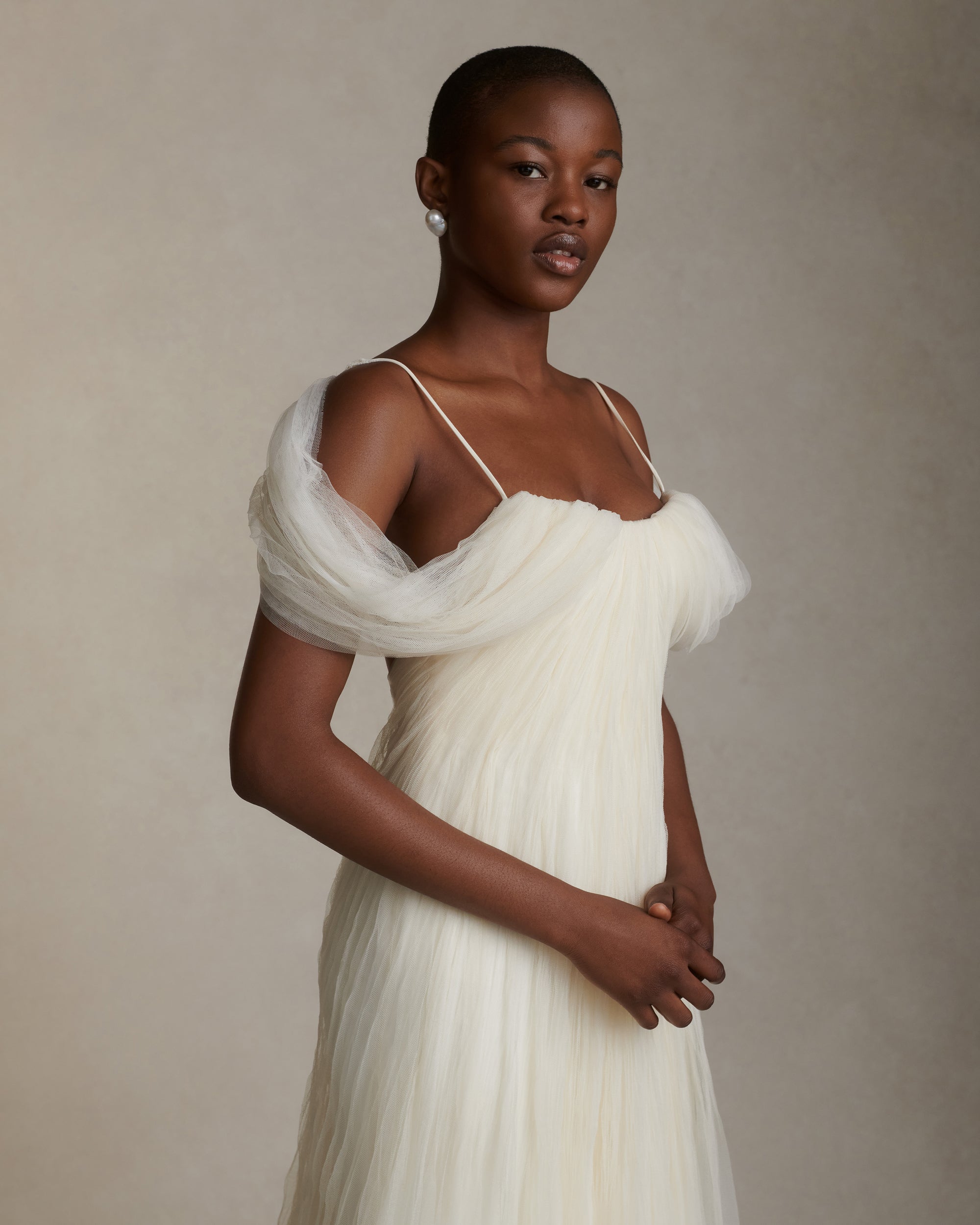 Pleated tulle swagged gown. Off the shoulder soft drapes releasing from center neckline to spaghetti strap back. Sunburst pleated, hand crinkled soft tulle through body and extending down center back for shape and movement. Soft internal bustier with side boning. Low center back zip, hook and eye closure.