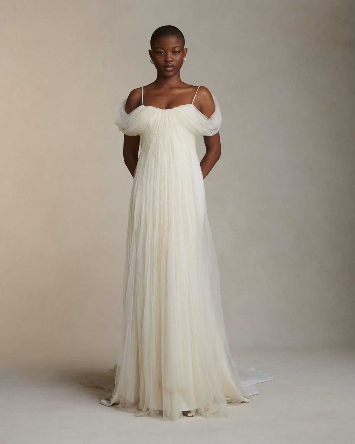 Pleated tulle swagged gown. Off the shoulder soft drapes releasing from center neckline to spaghetti strap back. Sunburst pleated, hand crinkled soft tulle through body and extending down center back for shape and movement. Soft internal bustier with side boning. Low center back zip, hook and eye closure.