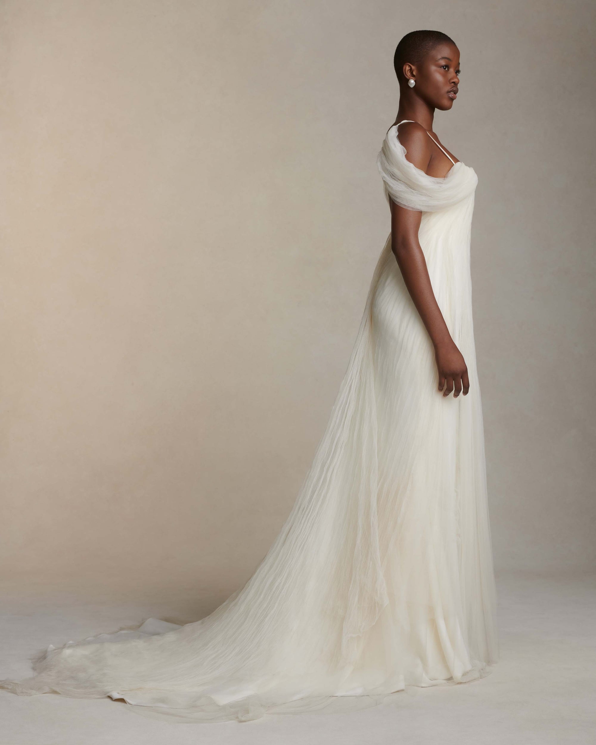 Pleated tulle swagged gown. Off the shoulder soft drapes releasing from center neckline to spaghetti strap back. Sunburst pleated, hand crinkled soft tulle through body and extending down center back for shape and movement. Soft internal bustier with side boning. Low center back zip, hook and eye closure.