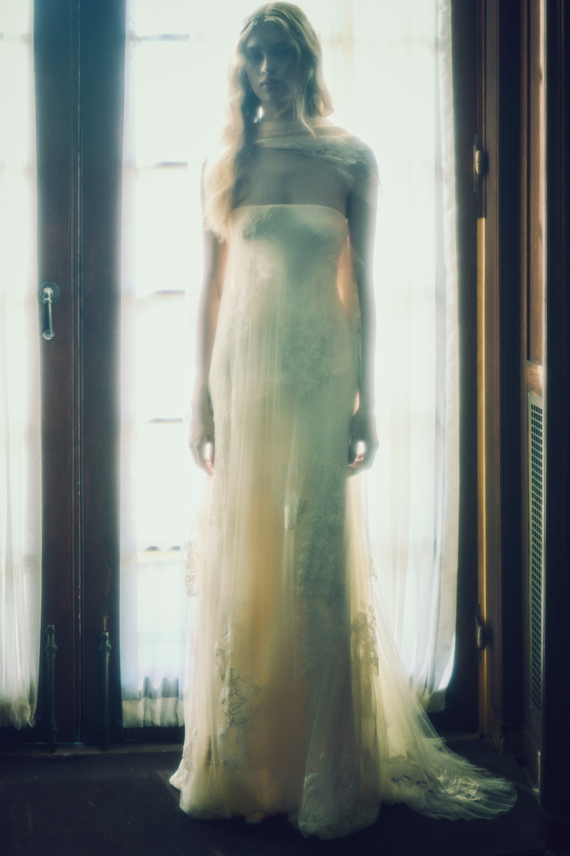 Strapless satin gown with soft tulle overlay decorated in hand cut corded and chantilly lace appliques. Asymmetric drape wraps gracefully across neck and shoulders falling into a scarf drape detail at low back. Bubble hem releases into train at back. Boned internal bustier with soft cups and center back zip closure.