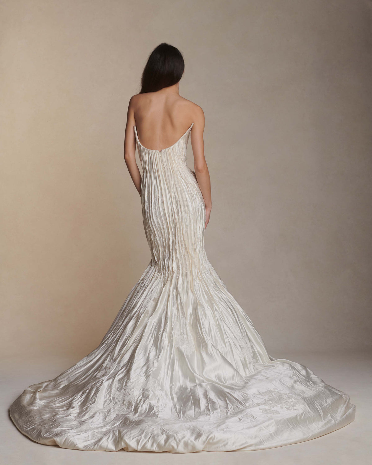 Silk wool hand crinkled gown fluted gown. Carved and sculpted strapless neckline. Hand appliquéd chantilly and corded lace motifs through body. Bubbled ankle grazing hem at front graduating into dramatic bubbled train. Soft internal corset with boning and center back zip closure.