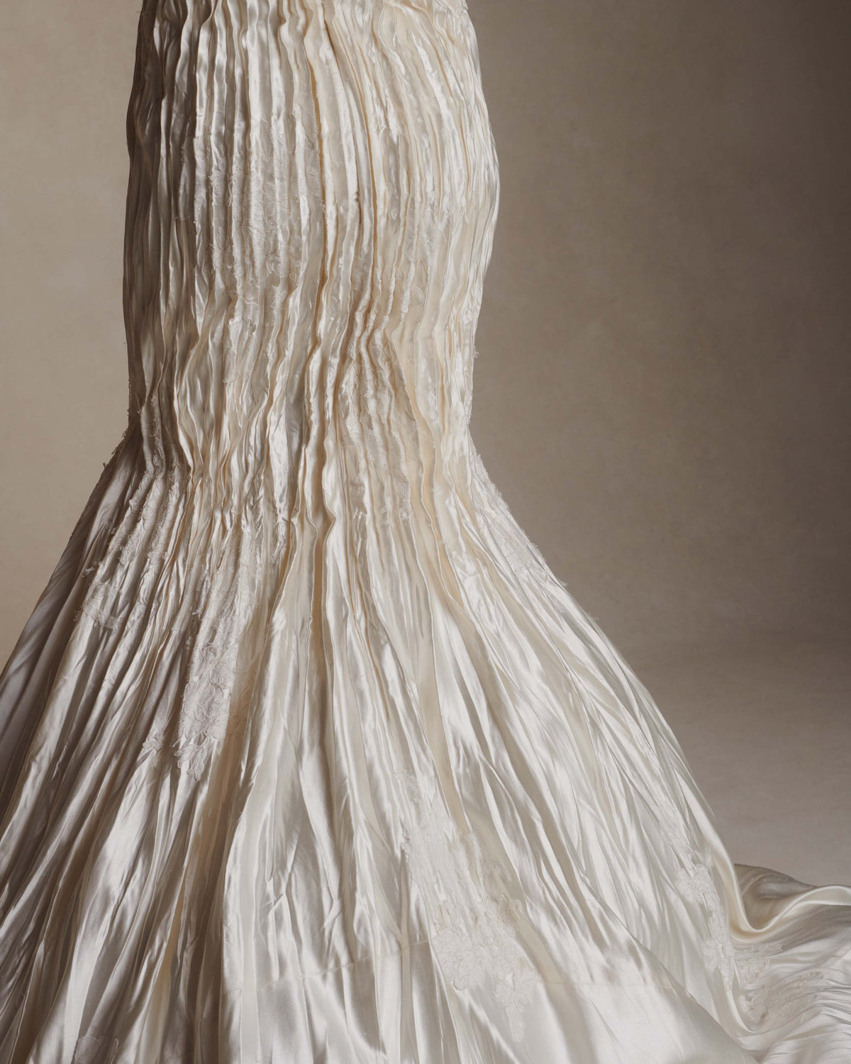 Silk wool hand crinkled gown fluted gown. Carved and sculpted strapless neckline. Hand appliquéd chantilly and corded lace motifs through body. Bubbled ankle grazing hem at front graduating into dramatic bubbled train. Soft internal corset with boning and center back zip closure.