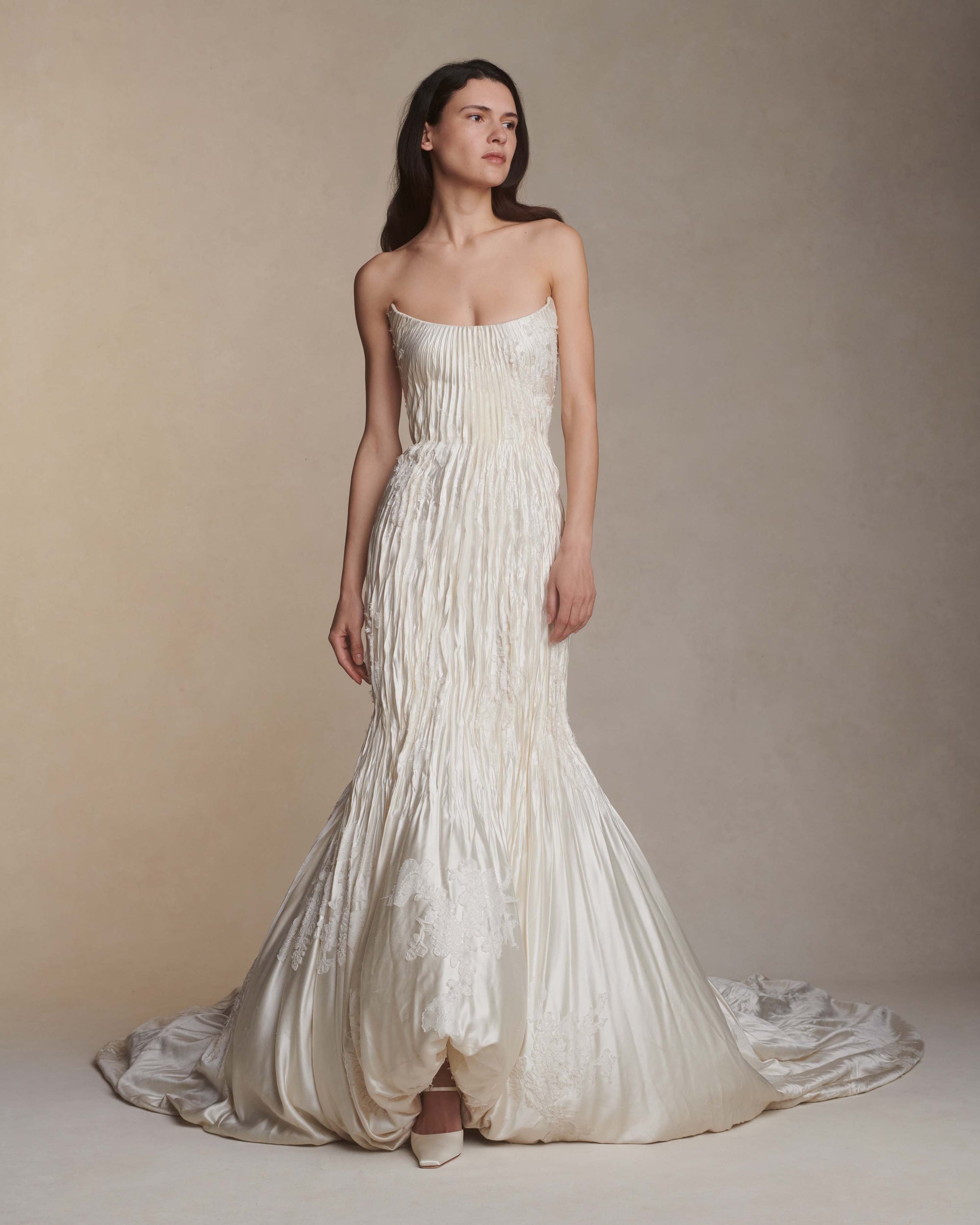 Silk wool hand crinkled gown fluted gown. Carved and sculpted strapless neckline. Hand appliquéd chantilly and corded lace motifs through body. Bubbled ankle grazing hem at front graduating into dramatic bubbled train. Soft internal corset with boning and center back zip closure.