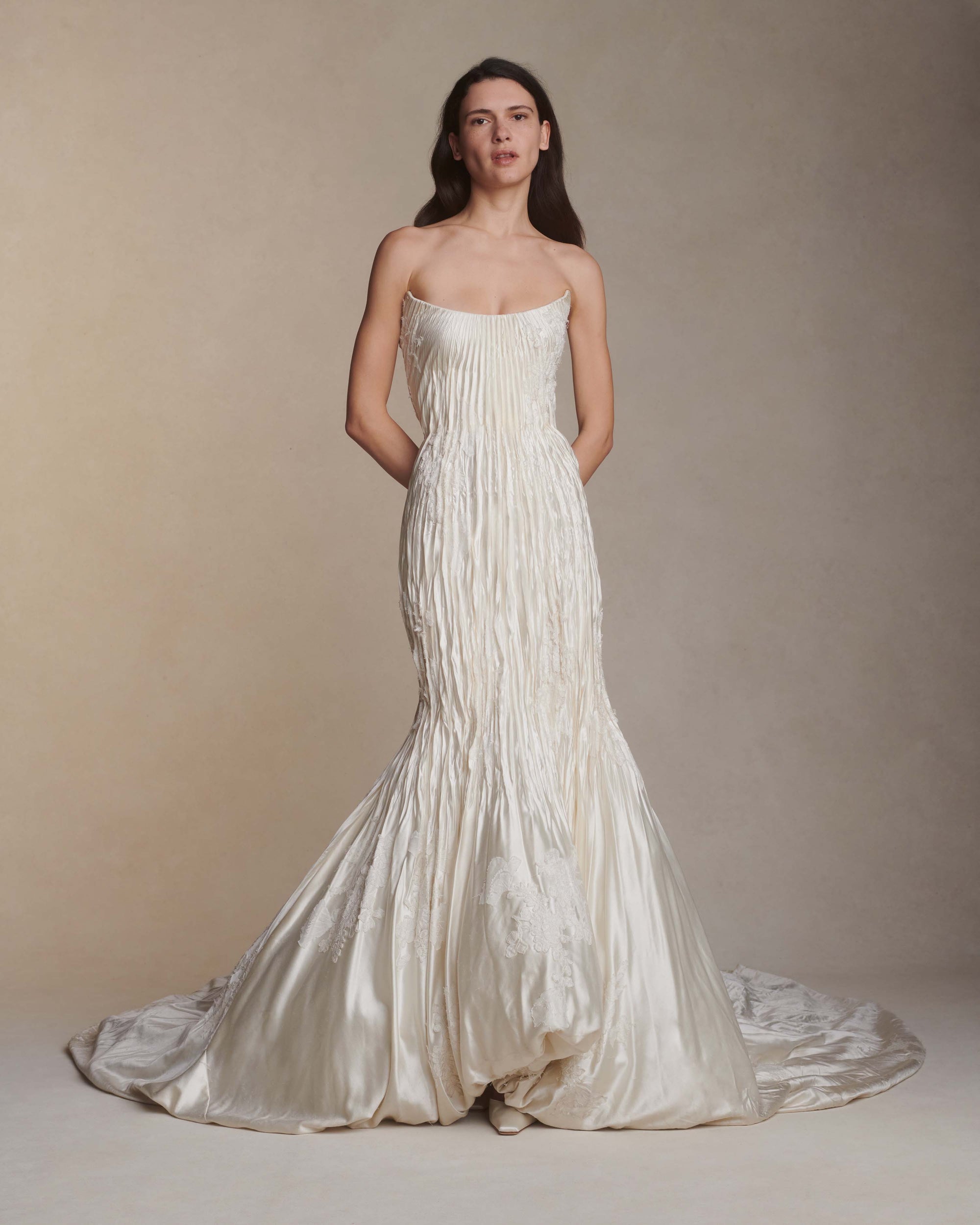 Silk wool hand crinkled gown fluted gown. Carved and sculpted strapless neckline. Hand appliquéd chantilly and corded lace motifs through body. Bubbled ankle grazing hem at front graduating into dramatic bubbled train. Soft internal corset with boning and center back zip closure.