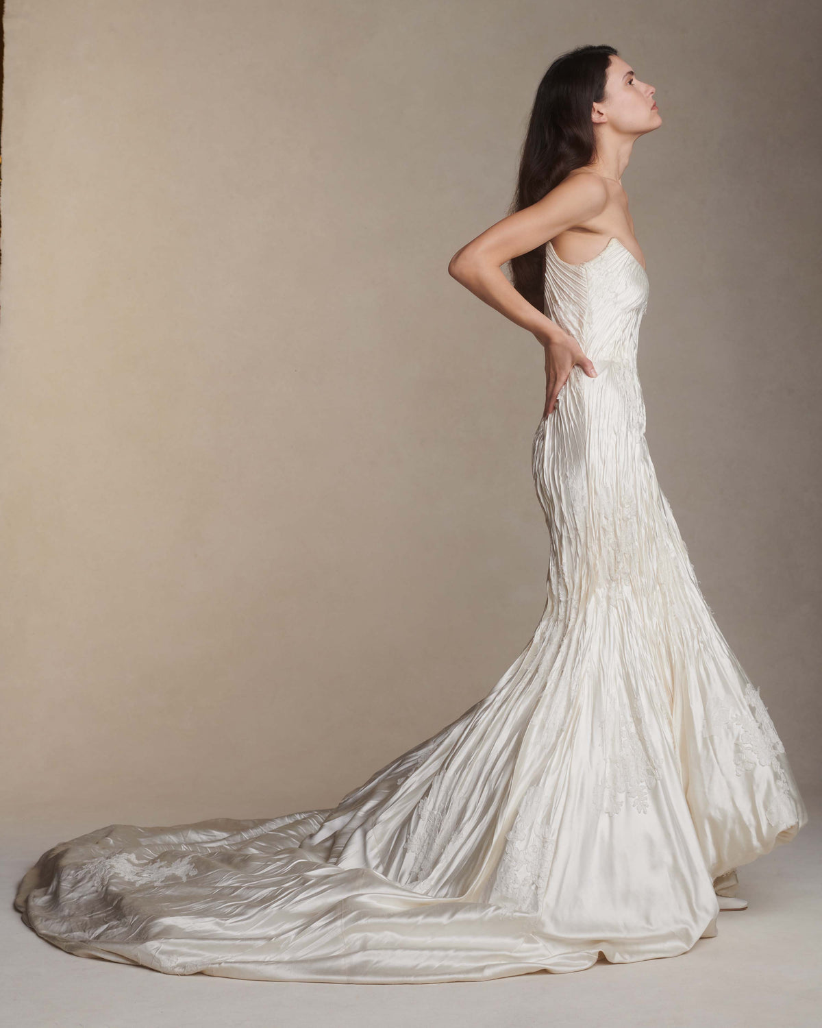 Silk wool hand crinkled gown fluted gown. Carved and sculpted strapless neckline. Hand appliquéd chantilly and corded lace motifs through body. Bubbled ankle grazing hem at front graduating into dramatic bubbled train. Soft internal corset with boning and center back zip closure.