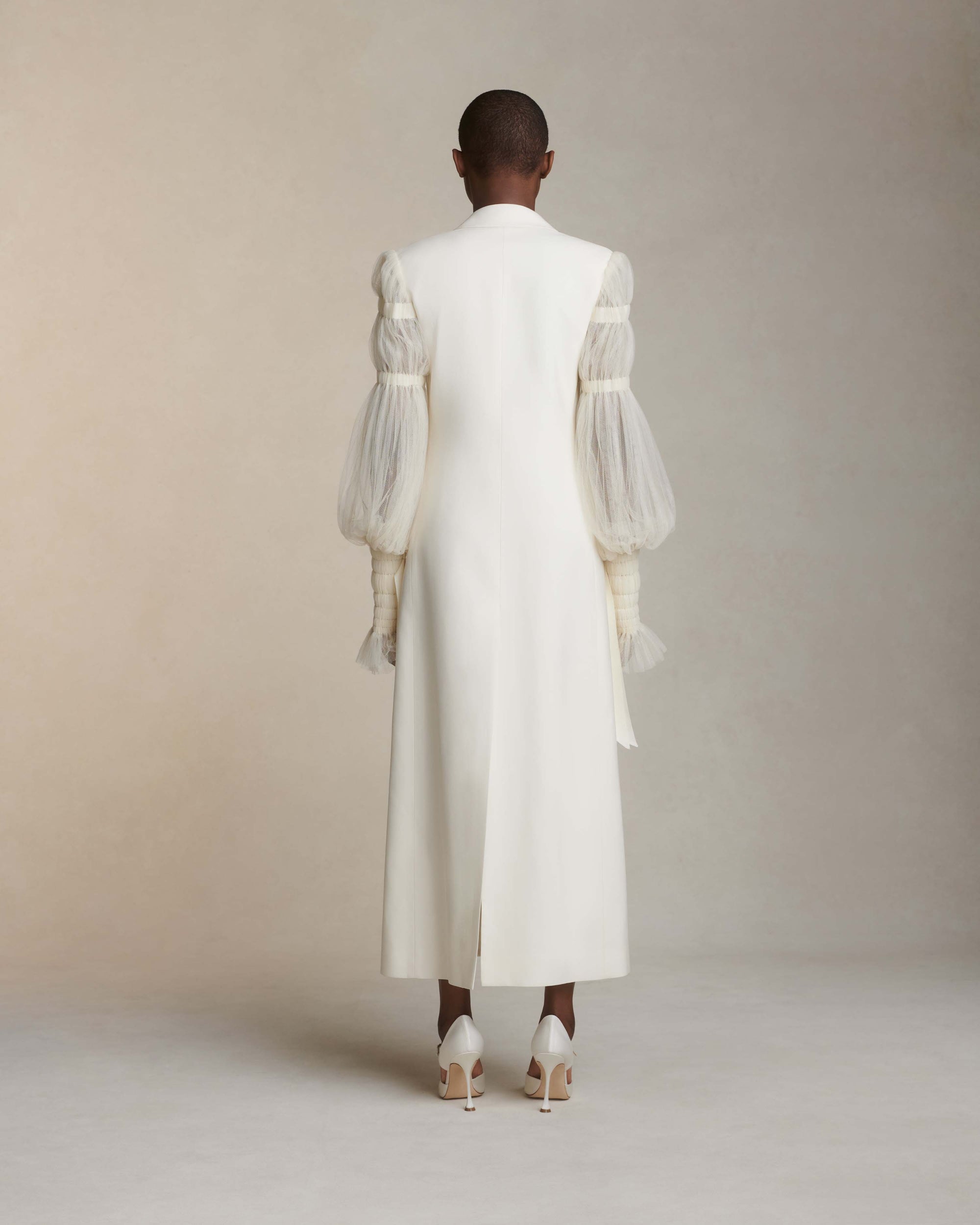Silk wool and smocked tulle overcoat. Peaked collar and tuxedo shine lapel with flap pocket at hips. Pleated soft tulle sleeves tunneled and accented with dripping grosgrain ribbons at elasticized wrists. Double breasted with button close.
