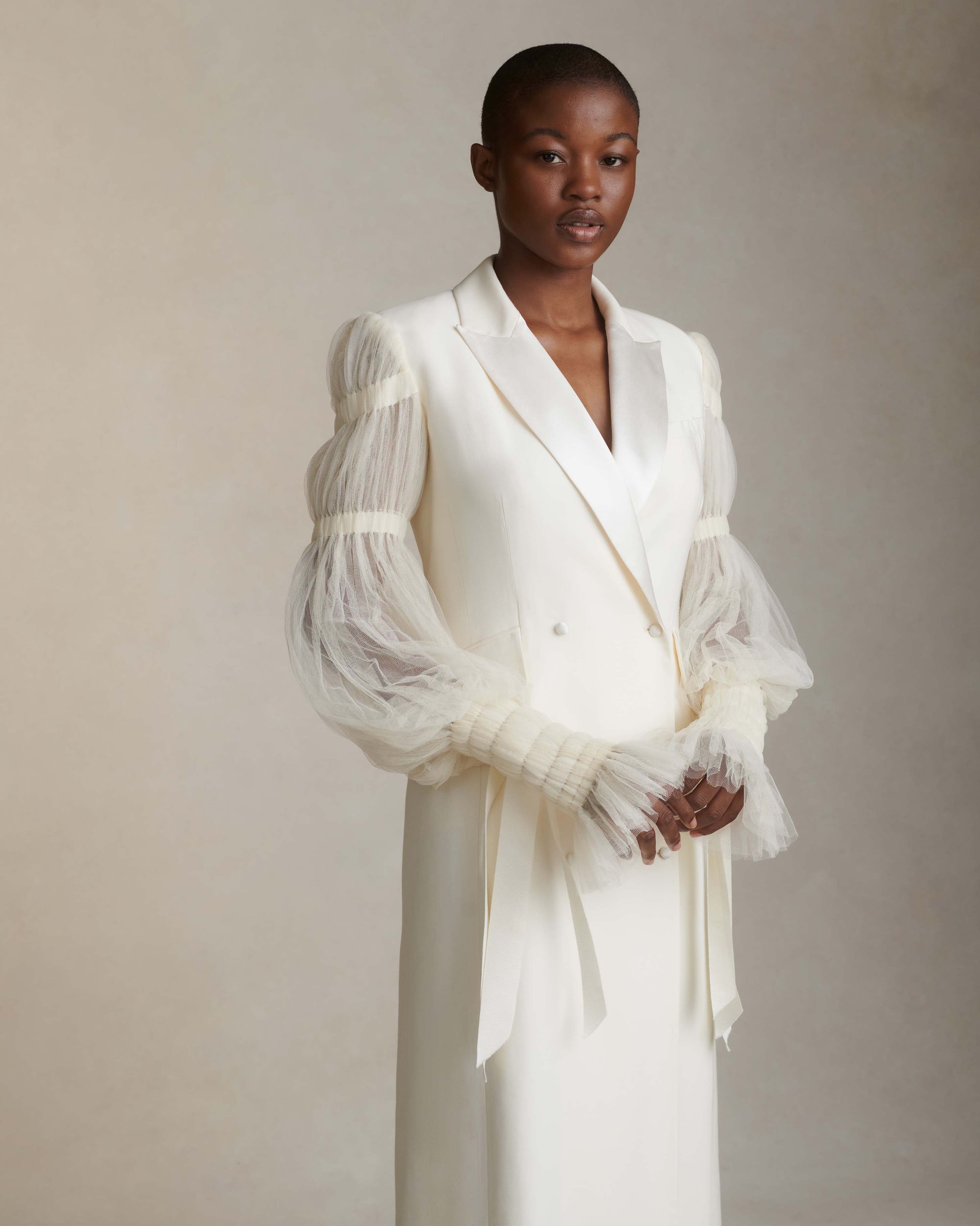 Silk wool and smocked tulle overcoat. Peaked collar and tuxedo shine lapel with flap pocket at hips. Pleated soft tulle sleeves tunneled and accented with dripping grosgrain ribbons at elasticized wrists. Double breasted with button close.