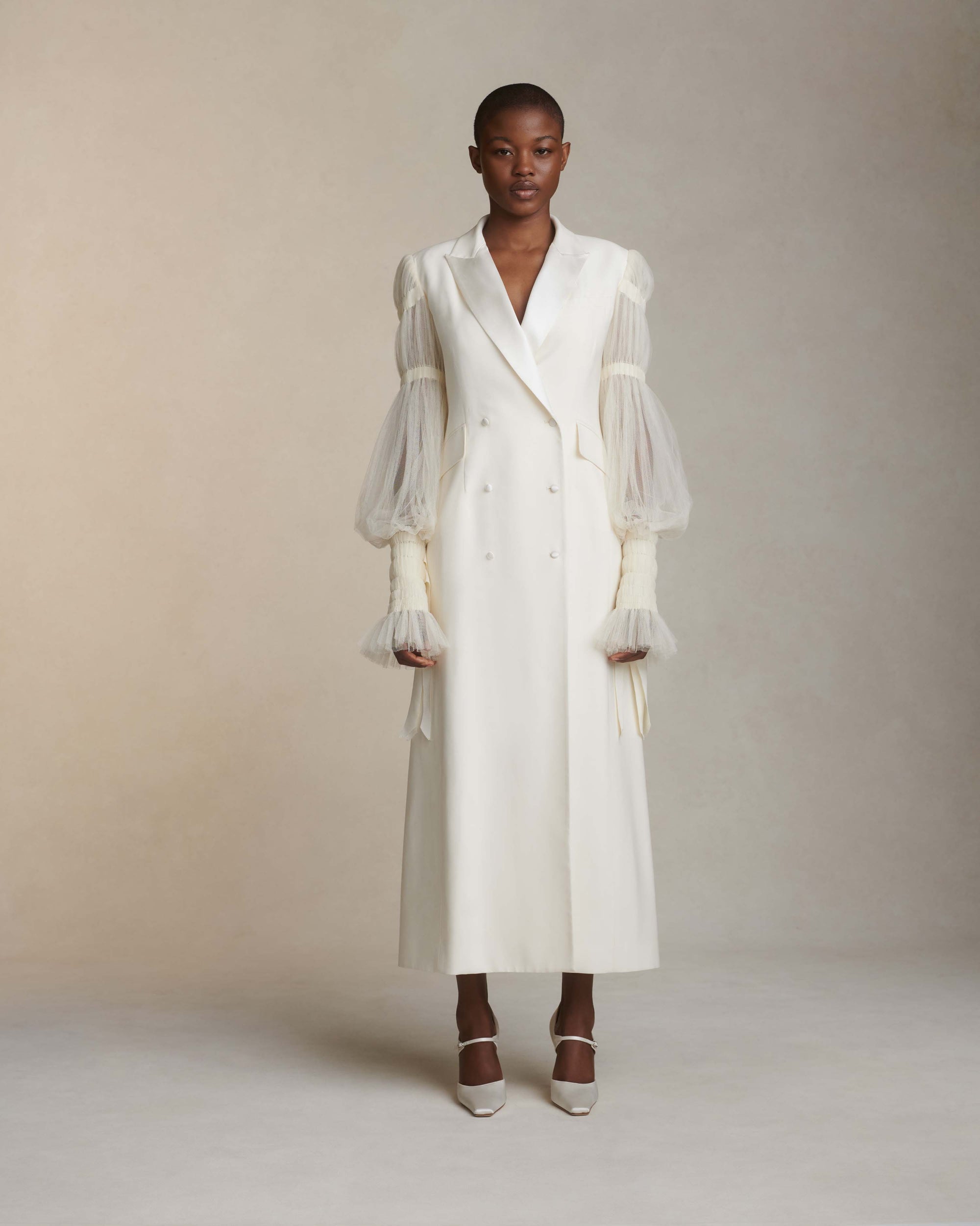 Silk wool and smocked tulle overcoat. Peaked collar and tuxedo shine lapel with flap pocket at hips. Pleated soft tulle sleeves tunneled and accented with dripping grosgrain ribbons at elasticized wrists. Double breasted with button close.