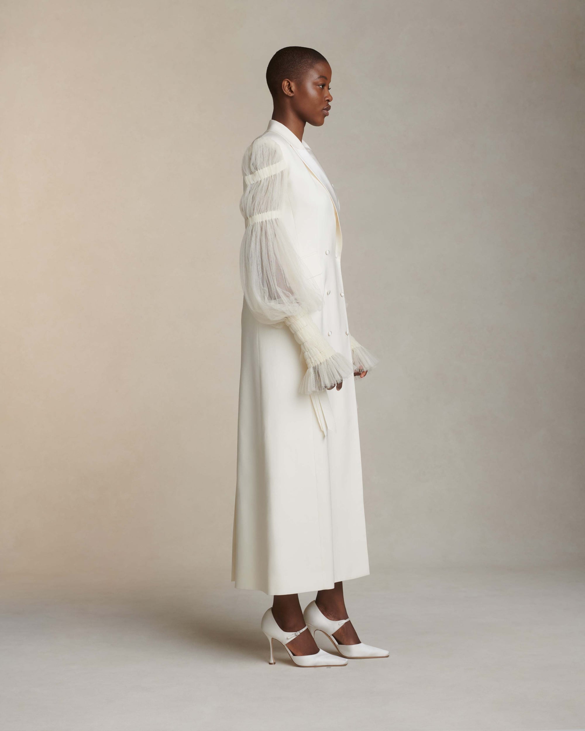 Silk wool and smocked tulle overcoat. Peaked collar and tuxedo shine lapel with flap pocket at hips. Pleated soft tulle sleeves tunneled and accented with dripping grosgrain ribbons at elasticized wrists. Double breasted with button close.